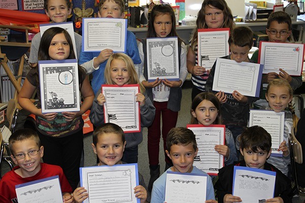 Pat Quinet’s third-grade class holds up their letters and art work for soldiers. Their work is included in care packages sent out by Gardiner Community Church.