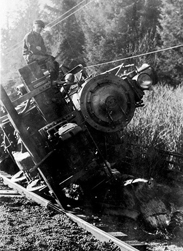 Men sit atop on pilot beam of an engine after a train wreck and derailment near Clallam Bay.