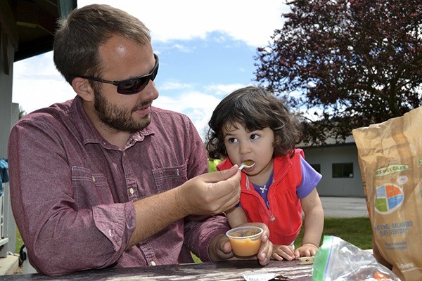 Tyler Sims of Sequim helps his 18-month daughter Sophia eat applesauce in Carrie Blake Park on June 16. The meal was one of many made free to children under 18 through the Summer Food Service Program at nine locations presented by the Boys & Girls Clubs of the Olympic Peninsula.
