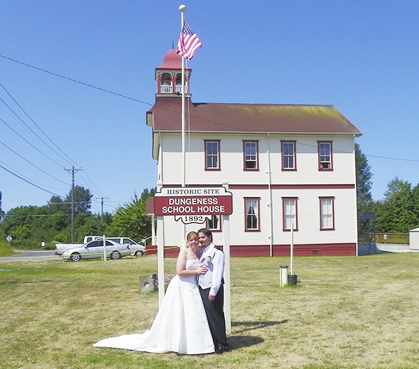 Standing below a replica of the 1971 Dungeness Schoolhouse sign which now graces the 1892 historical site are newlywed local residents