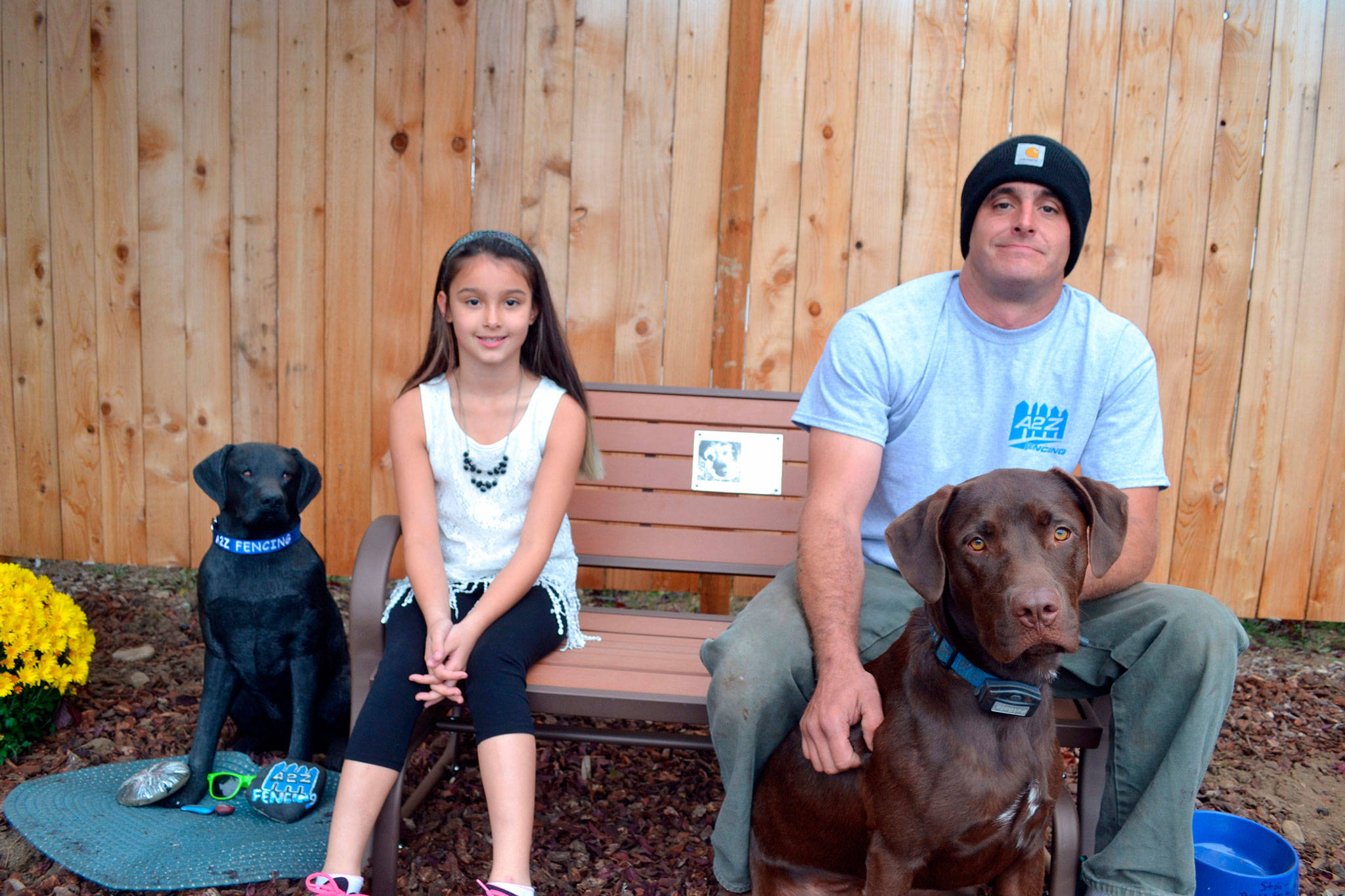 Alabama and her dad Kevin Cassidy sit on a bench with their dog Remington last October that memorializes family dog Stolli, who died on Aug. 31, 2016. The statue to the left was reported stolen Aug. 3 and recovered later in the day broken. Community members look to fund a replacement for the Cassidy family. Sequim Gazette file photo by Matthew Nash