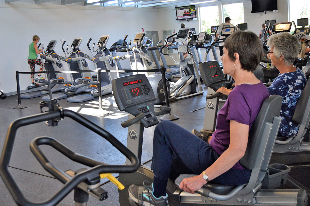 Mary Farley of Sequim and Linda Flores of Port Angeles cycle at the YMCA of Sequim on Aug. 28 during a workout with the Exercise and Thrive program. Sequim Gazette photo by Matthew Nash
