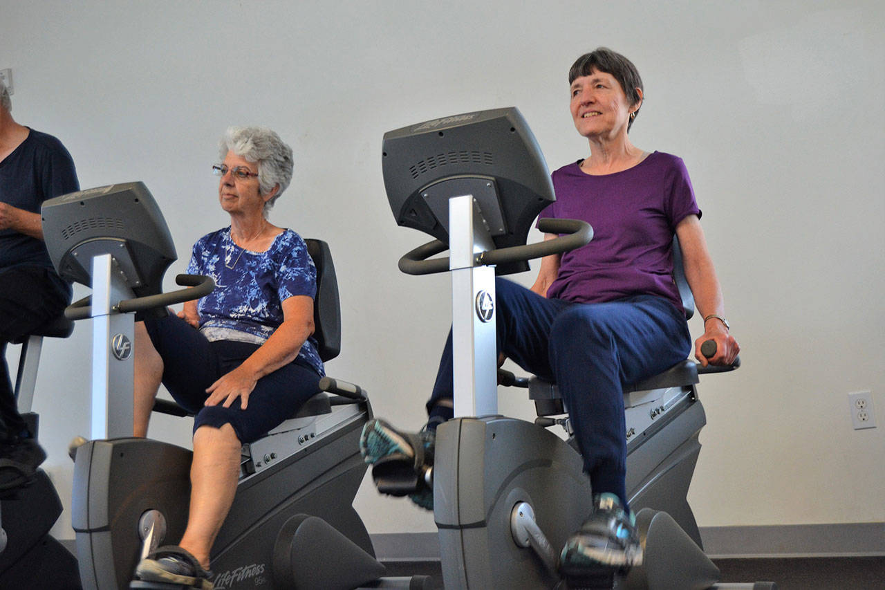 Linda Flores of Port Angeles, left, and Mary Farley of Sequim cycle at the YMCA of Sequim on Aug. 28 during a workout with the Exercise and Thrive program. Sequim Gazette photo by Matthew Nash