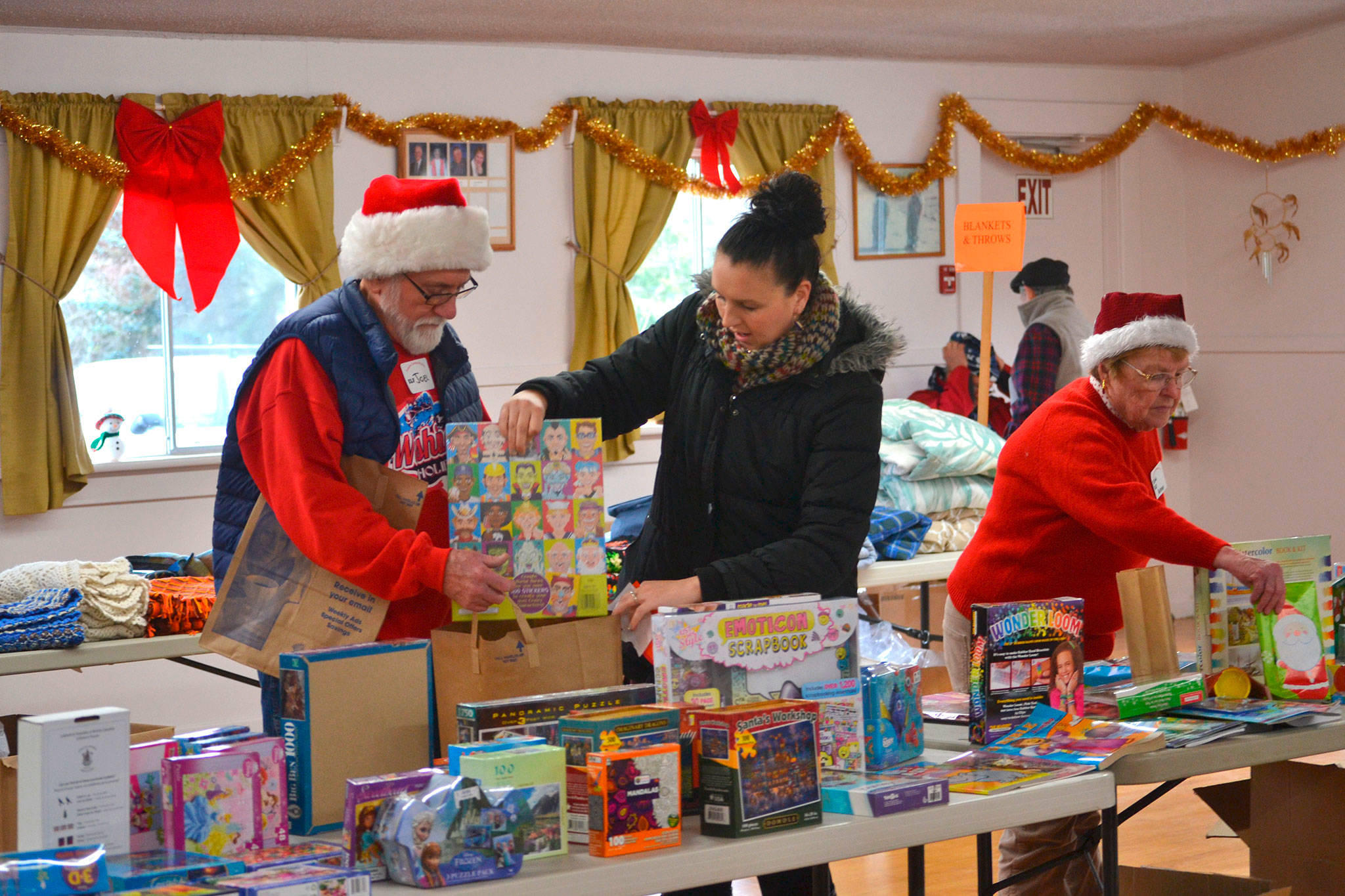 Volunteers Joel Ogden and Anne Notman with Sequim Community Aid help Sheena Touchard look for toys at last year’s Toys for Sequim Kids. Organizers said 400 children in Sequim received items from the event in 2016. This year, the event is set for Dec. 13, at the Sequim Prairie Grange. Sequim Gazette file photo by Matthew Nash