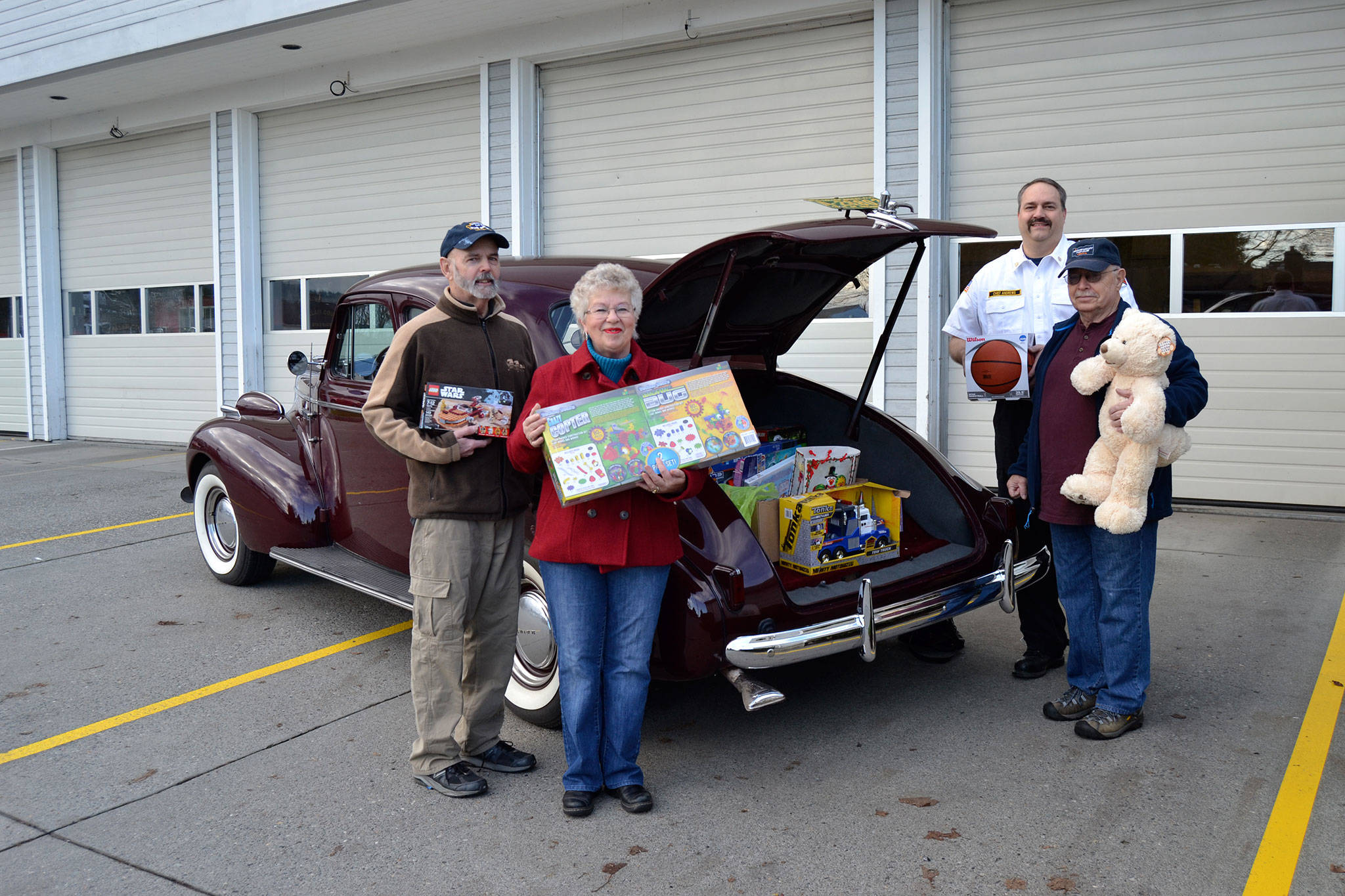 Members of the Sequim Valley Car Club, from left, Ralph Elston, Diane McIntosh, Fire Chief Ben Andrews with Clallam County Fire District 3, and David McIntosh stand with toys that filled Elston’s 1939 Buick for Toys for Sequim Kids. Sequim Gazette photo by Matthew Nash