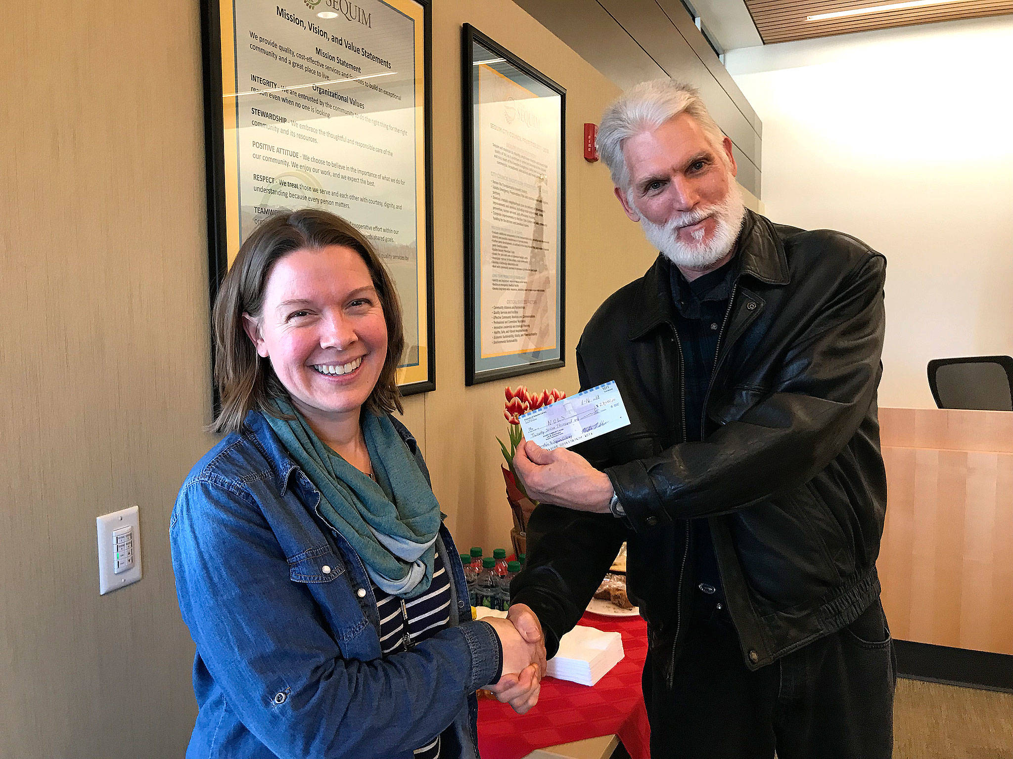 Emily Sly, Sequim Library’s branch manager, accepts a $27,000 check on Jan. 16 inside the Sequim Civic Center from Martin Shaw, treasurer for the Friends of Sequim Library. The donation comes from the Friends’ group’s monthly book sale and permanent sale inside the Sequim Library. Funds support the library’s entire program schedule, Sly said. Submitted photo