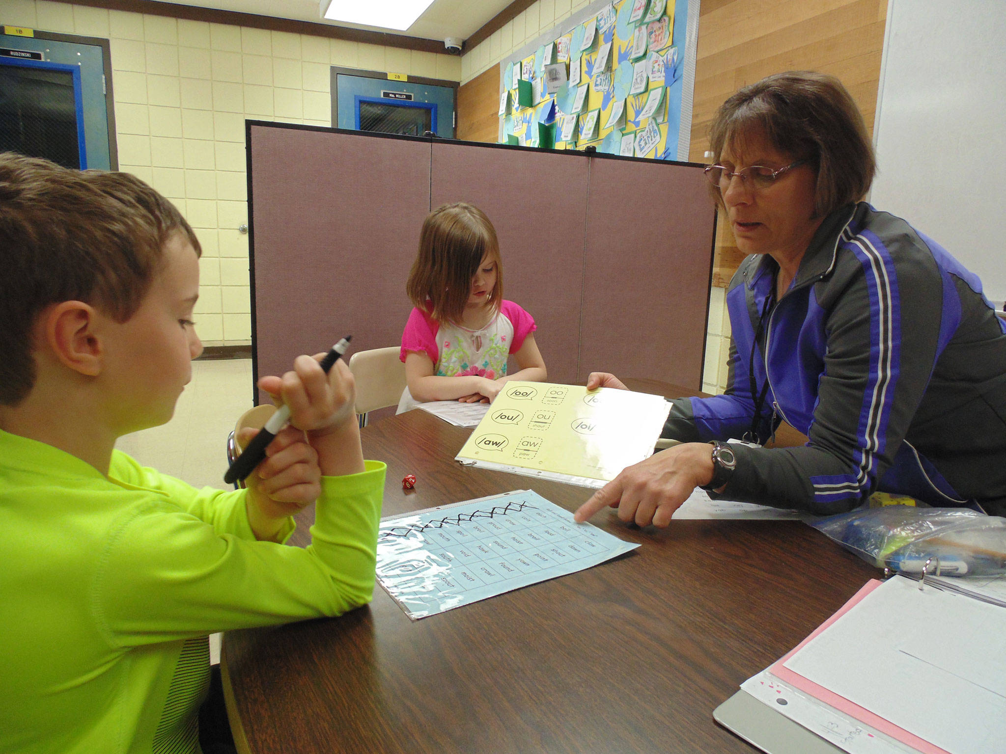 Paraeducators in Sequim School District already meet new paraeducator employment requirements which allow paraeducators to switch between duties and programs. Reading paraeducator Jan Webb works with Xavier Devlin and Alexia Brock at Helen Haller Elementary School. Submitted photo