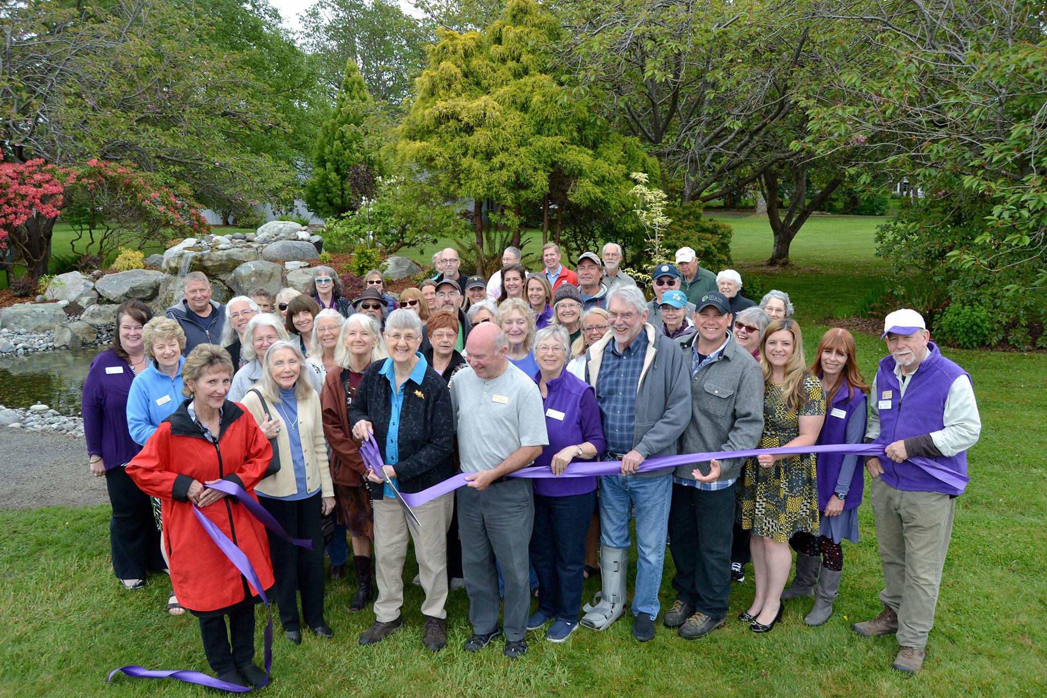 Priscilla Hudson, Sequim Prairie Garden Club member/historian, cuts the ribbon on May 16 to the refurbished fountain in Pioneer Memorial Park. She’s surrounded by dozens of community members including family members of the Lotzgesell family with Henry Lotzgesell donating a sizable amount in 1965 in honor of his wife Hazel to see the project come to fruition. Sequim Gazette photo by Matthew Nash