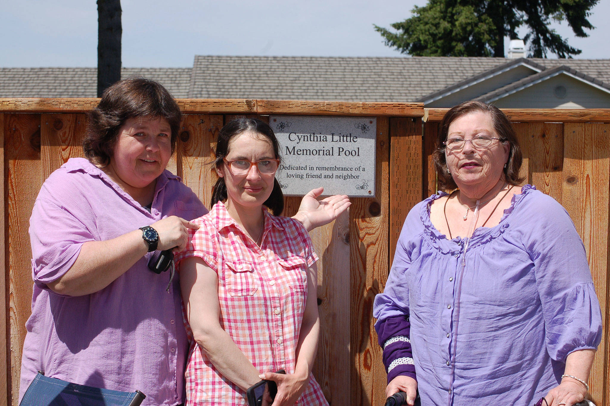 Close friends of Cynthia Little, such as Bernie Philbin, left, CASA volunteer Emma Jones and Maggie Philbin, stand next to Little’s dedication plaque at the Sunland Golf & Country Club pool on June 17.