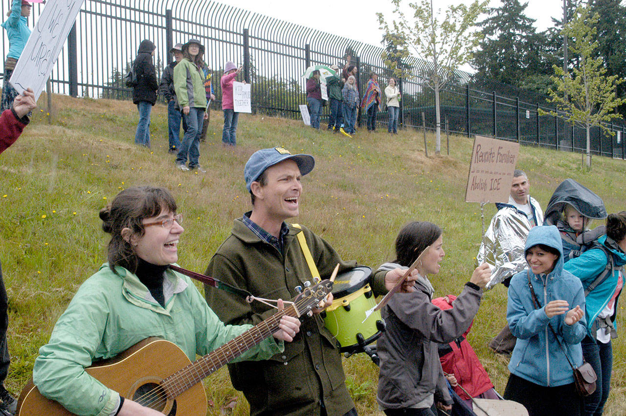 Ashley Kramer and Joe Bridge of Sequim play music at the Families Belong Together rally near the U.S. Border Patrol building in Port Angeles on Saturday. Similar rallies were taking place across the country to protest federal immigration policies. (Rob Ollikainen/Peninsula Daily News)
