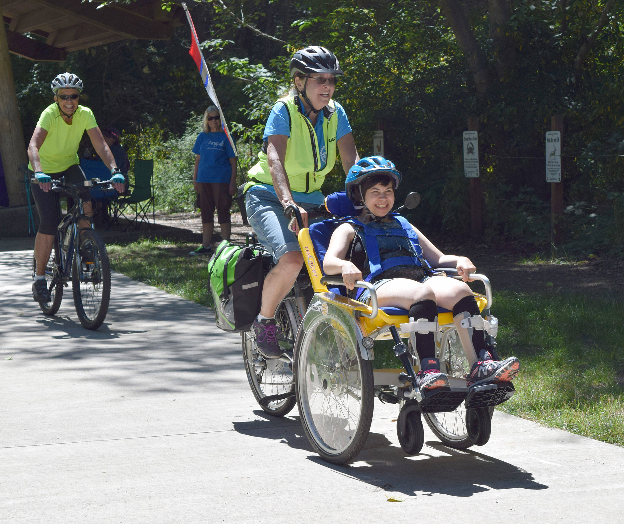Piloted by Sequim Wheelers volunteer Elaine Cates, center, Kaitlyn Winn, foreground, enjoyed a ride on a duet wheelchair bicycle during a Clallam Mosaic sponsored field trip to Railroad Bridge Park on July 13. Riding as a safety was Sequim Wheelers volunteer Michele Fraker. Submitted photo