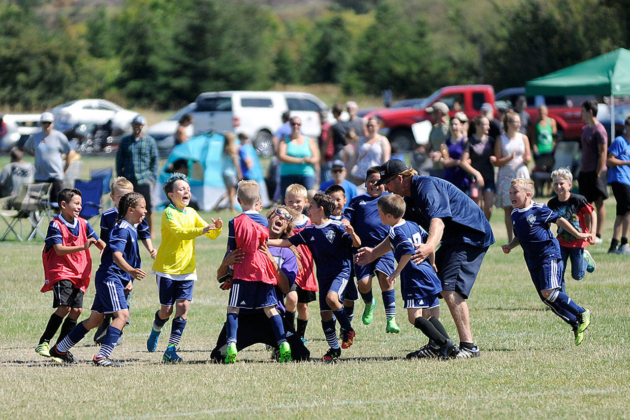 Storm King BU10 teammates and coaches rally around Trevor Goff after the player — who also handled goalkeeper responsibilities for the penalty kicks — knocked in the game-winner to topple Harbor Premier B10 Green at the Dungeness Cup on Aug. 5.                                 Sequim Gazette photo by Michael Dashiell