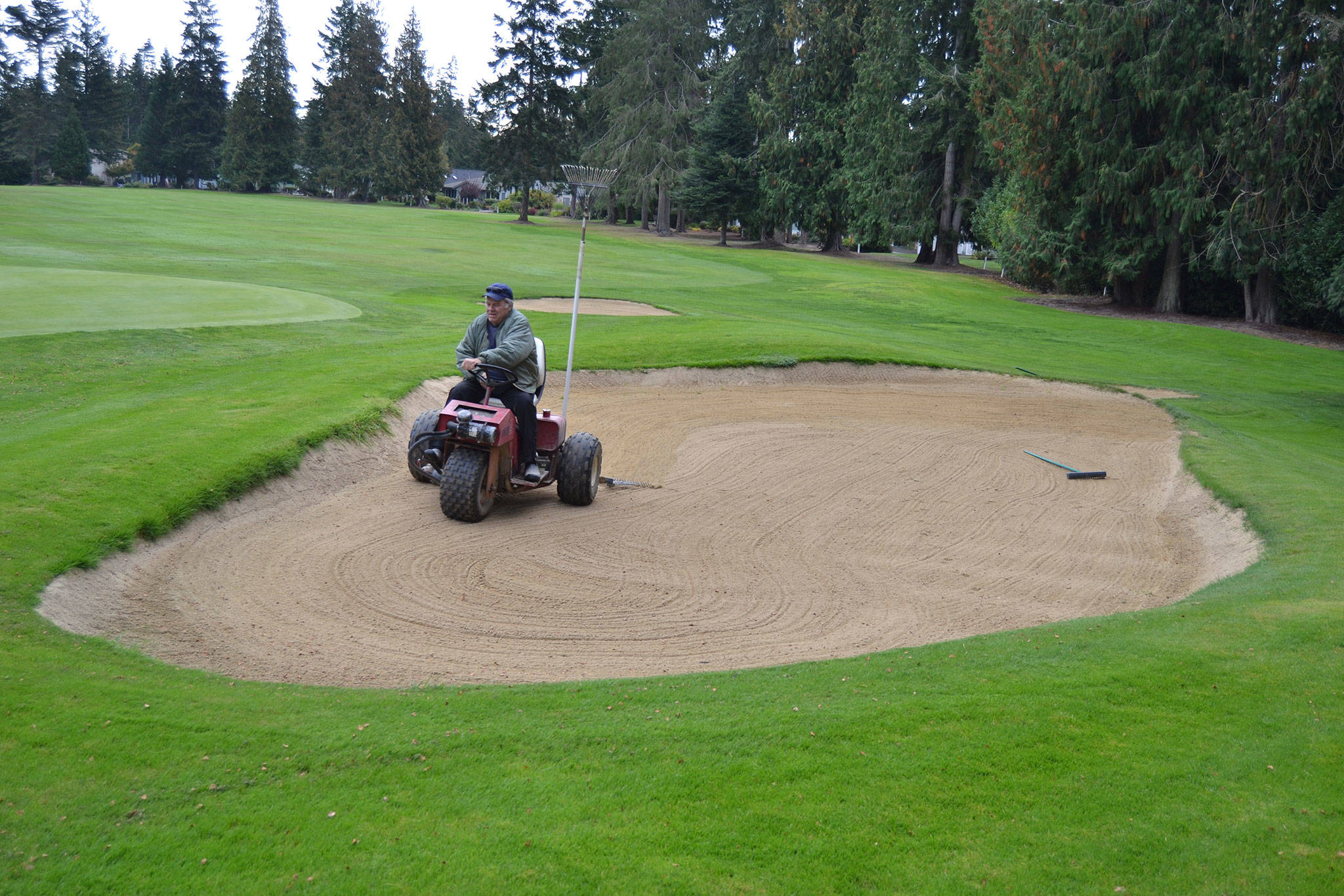 Thomas Matney, a maintenance worker for Sunland Golf & Country Club, rakes the sand on hole 18 on Sept. 25. The course now opens to the public after 2 p.m. weekdays and on Fridays after noon. Sequim Gazette photo by Matthew Nash