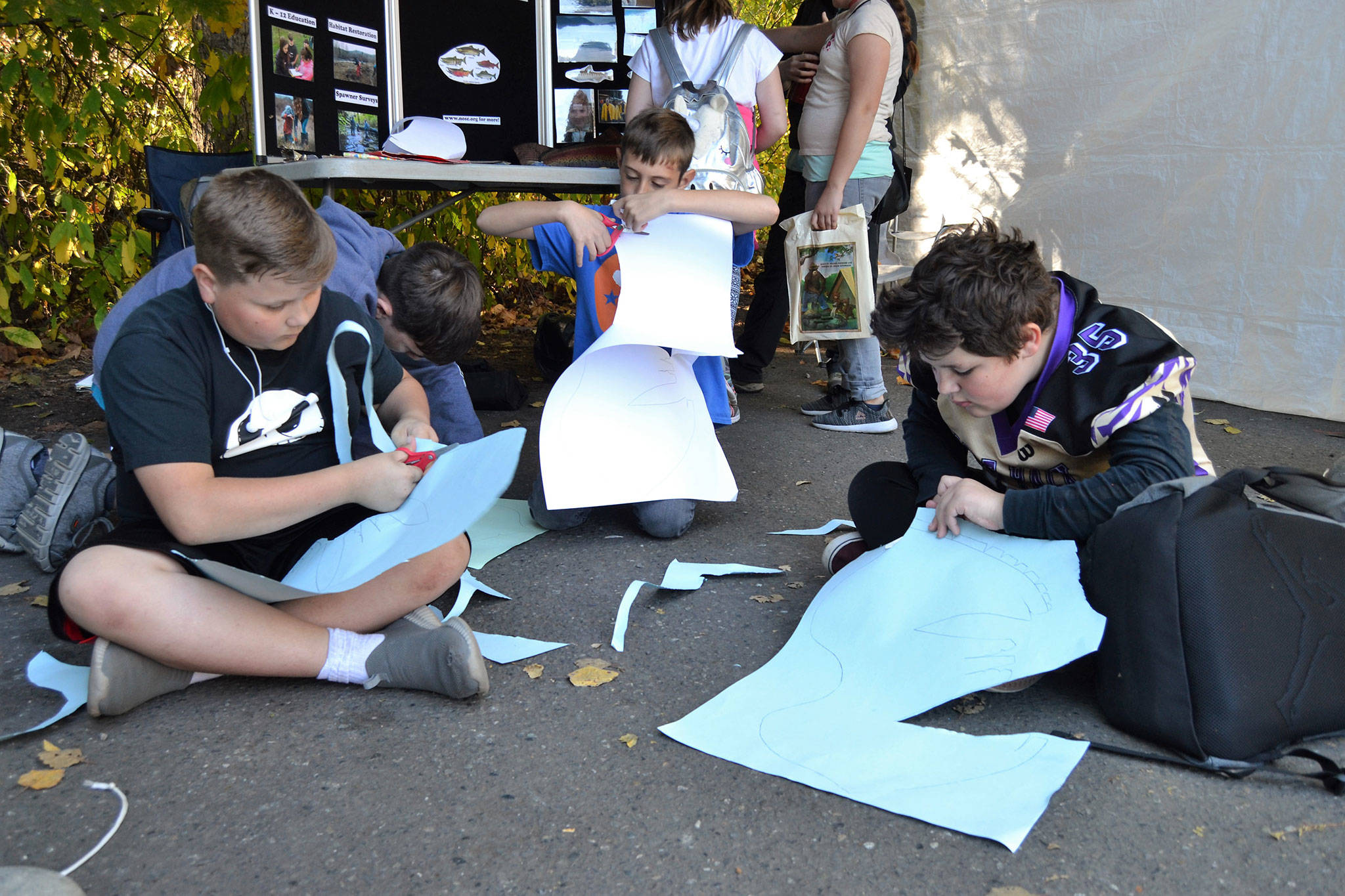 Fifth graders, from left, Justin Anderson, 10, Sammy Cobb, 10, and Jaden Rinaldo-Hollingsworth, 12, cut out fish hats at the North Olympic Salmon Coalition’s booth near the Dungeness River Railroad Bridge. Sequim Gazette photo by Matthew Nash