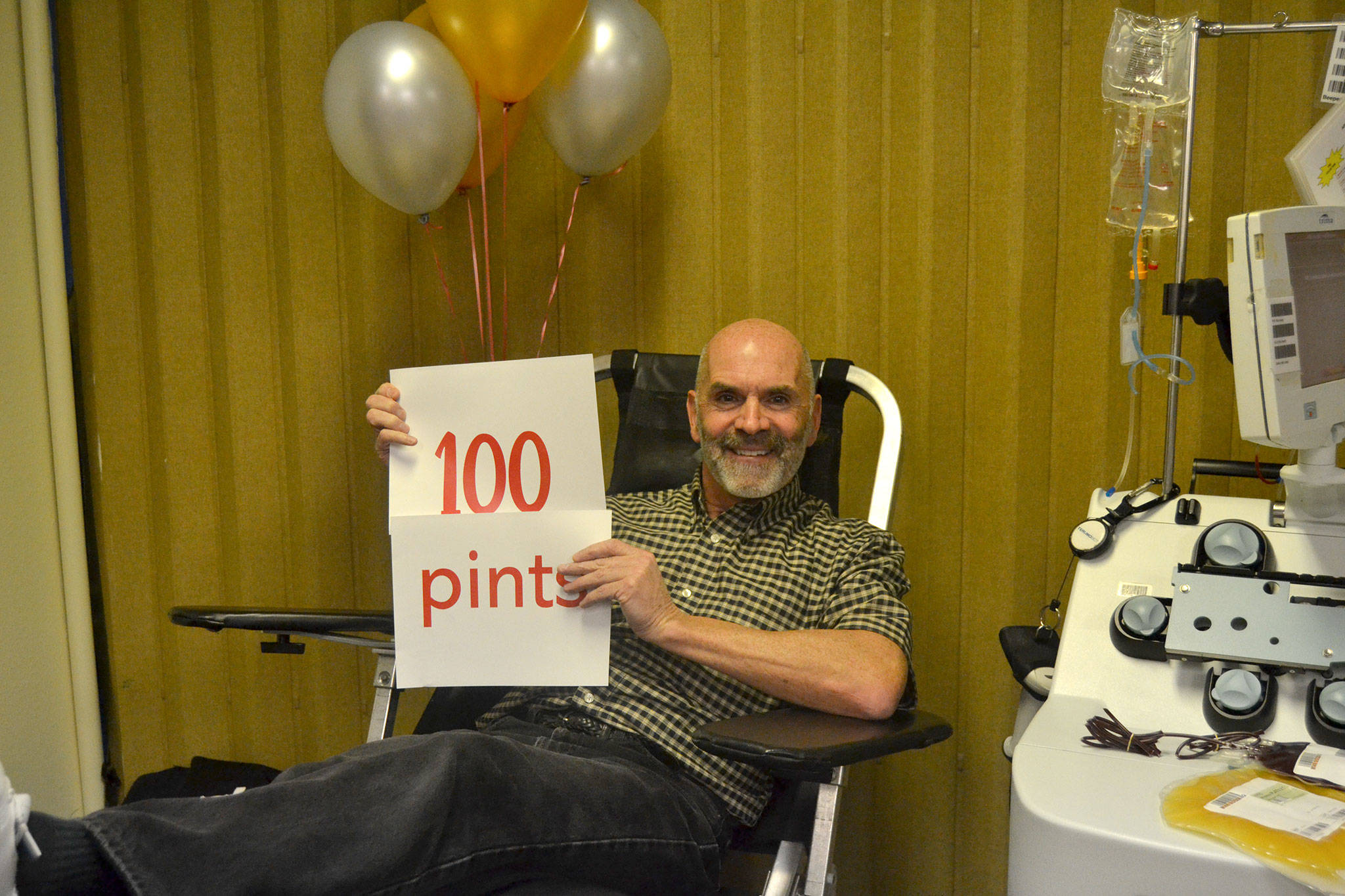 Friend and coworker Gigi Marunde surprises Doug Brundage with balloons and a sign for donating 100 pints of blood and platelets on Nov. 8. Brundage said a coworker being diagnosed with leukemia inspired him to continue giving blood. Sequim Gazette photo by Matthew Nash