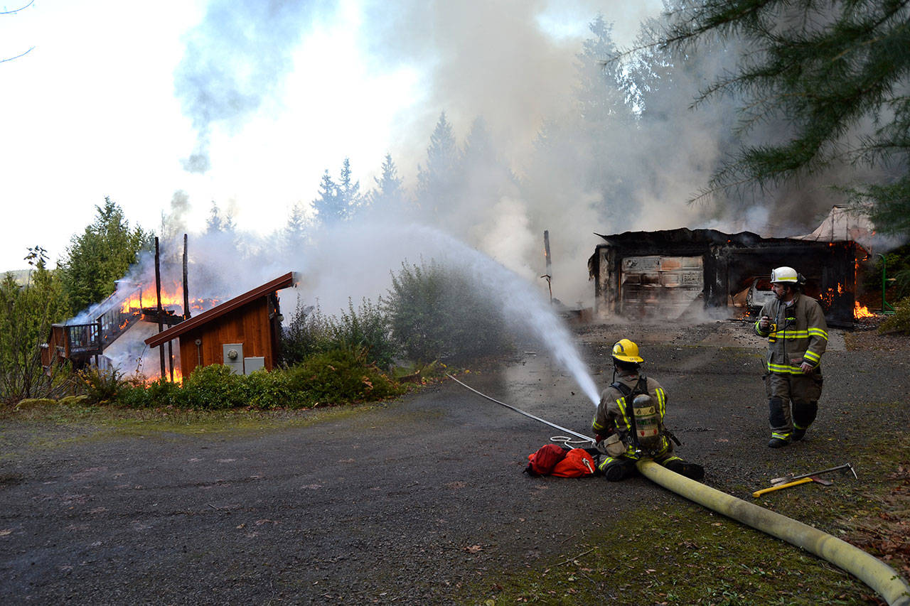 Firefighter/EMT Kjel Skov sprays down flames with direction from Assistant Fire Chief Tony Hudson on Dec. 3 as a fire burns a Blyn Home. Sequim Gazette photo by Matthew Nash