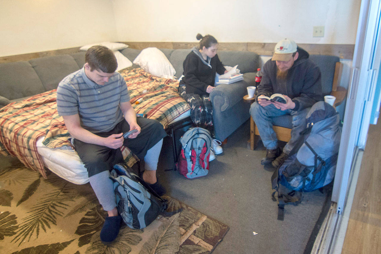 Jacob Olson, left, looks through Magic the Gathering cards while Colleen and Ted Chapman read at Serenity House of Clallam County’s night-by-night shelter Thursday. The shelter is open 24/7 while temperatures stay below freezing. (Jesse Major/Peninsula Daily News)