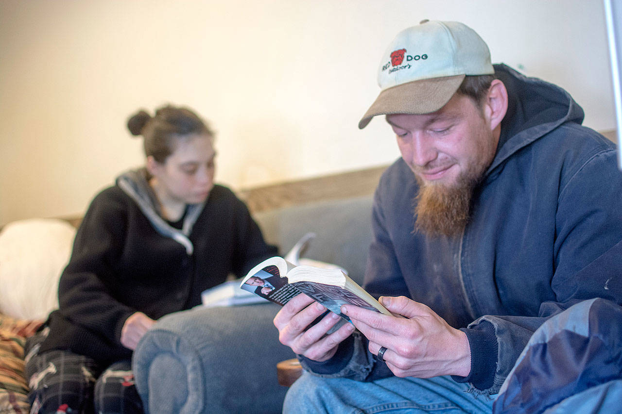Colleen and Ted Chapman read together while staying at Serenity House of Clallam County’s night-by-night shelter Thursday. The shelter is open 24/7 while temperatures stay below freezing. (Jesse Major/Peninsula Daily News)