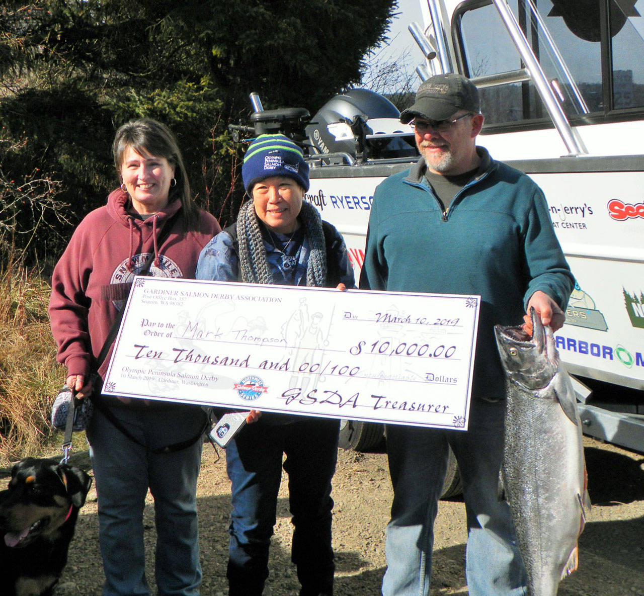 Mark Thompson, right, holds his 19.35-pound blackmouth salmon that earned the $10,000 first prize at the 2019 Olympic Peninsula Salmon Derby. His wife Kristi Thompson is at left, with Kathy Watrous, Gardiner Salmon Derby Association President, holding Thompson’s $10,000 check. The trio is standing in front of the 2019 Northwest Salmon Derby Series Grand Prize Boat valued at $75,000; each derby entrant received an entry for the boat drawing which will be held in September. Submitted photo