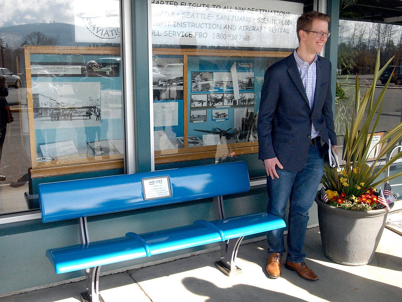 U.S. Rep. Derek Kilmer, D-Gig Harbor, stands next to a composite fiber bench dedicated to him for his efforts on legislation which secured government funding to keep the full runway open at William R. Fairchild International Airport in Port Angeles during Kilmer’s visit with community leaders at the airport. (Keith Thorpe/Peninsula Daily News)
