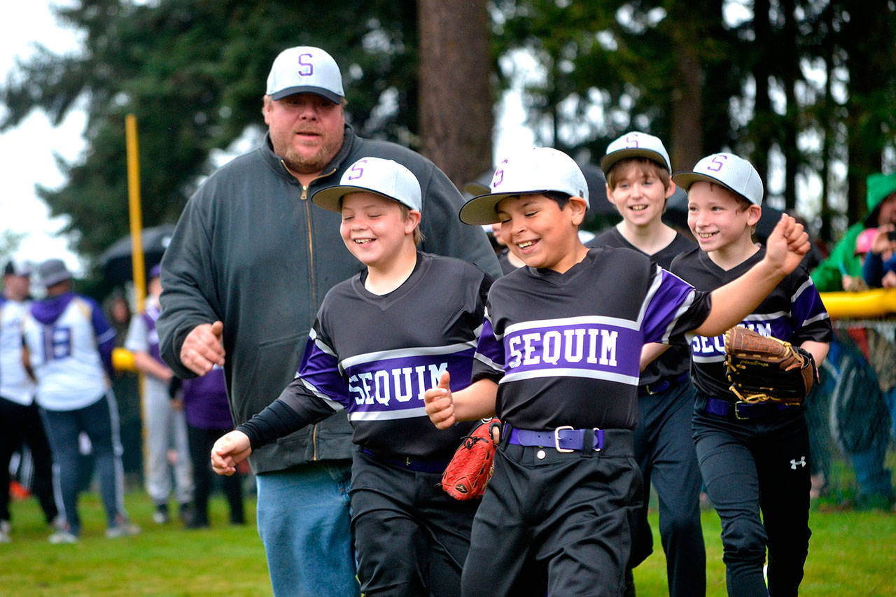 Olympic Game Farm Minor League players, from left, Kaleb Delph, 10, Domink Johnson, 9, Cooper Sharpe, 11, and Brody Lewis, 10, race their coach Quentin Delph during the Sequim Little League’s Players Procession. Each team was introduced in front of hundreds of spectators at Dr. James Standard Memorial Little League Park.