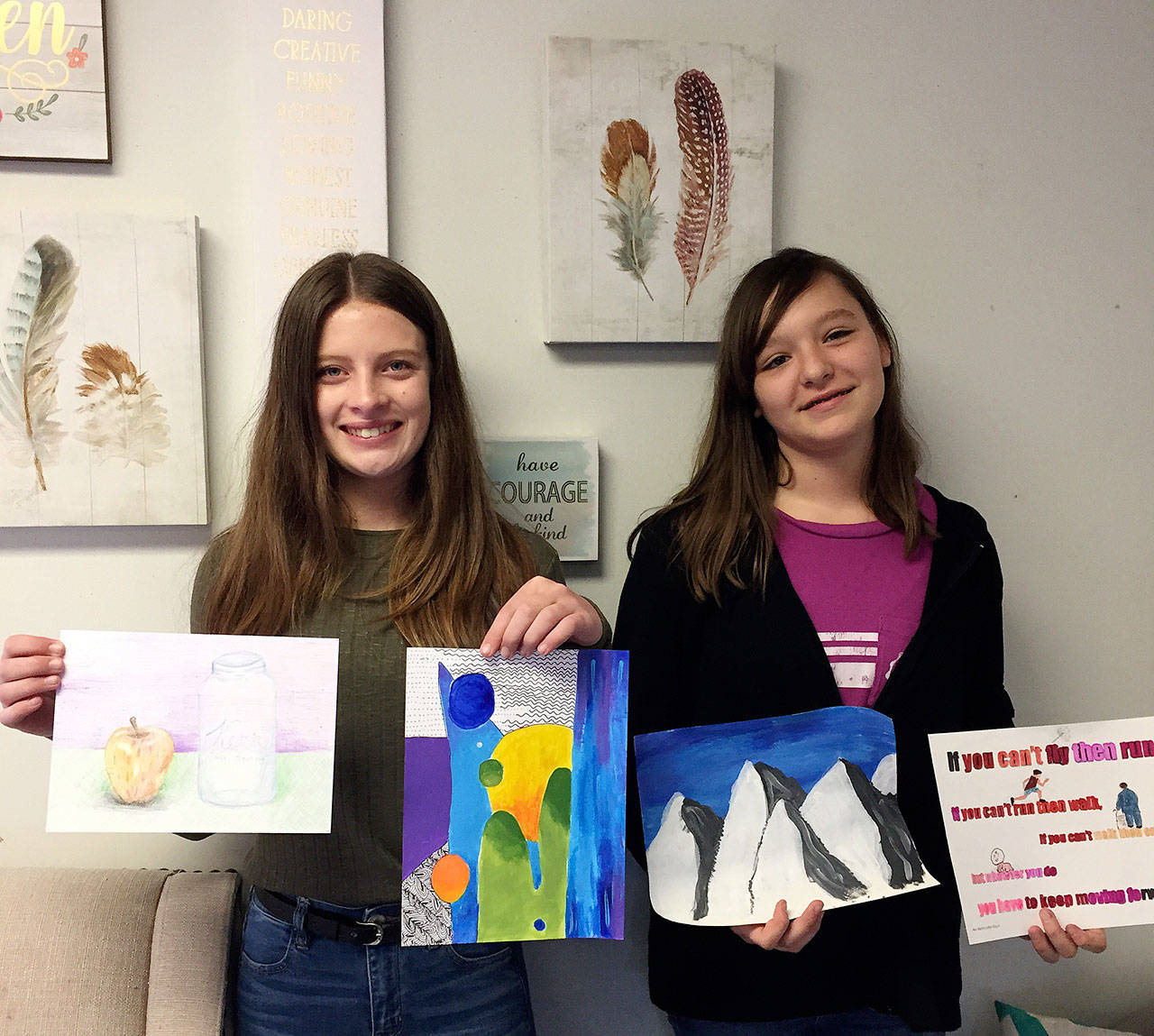 Olympic Christian School students Ellie Smith, left, and Coco Broker display some of their artwork at the school’s recent Art Festival. Smith took top honors in the seventh-/eighth-grade division with her “Galactic Gradients” painting, while Broker placed second with her painting, “The Magnificent Mountains.” Photo courtesy of Olympic Christian School