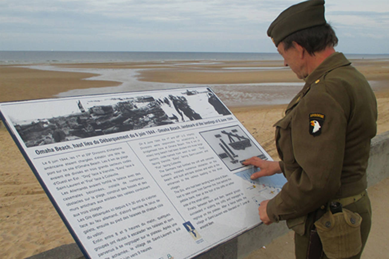 An unidentified World War II reenactor in uniform reading a commemorative sign overlooking the Normandy beach designated “Omaha Beach” by Allied strategists for the D-Day invasion. Photo submitted by Mac Macdonald.