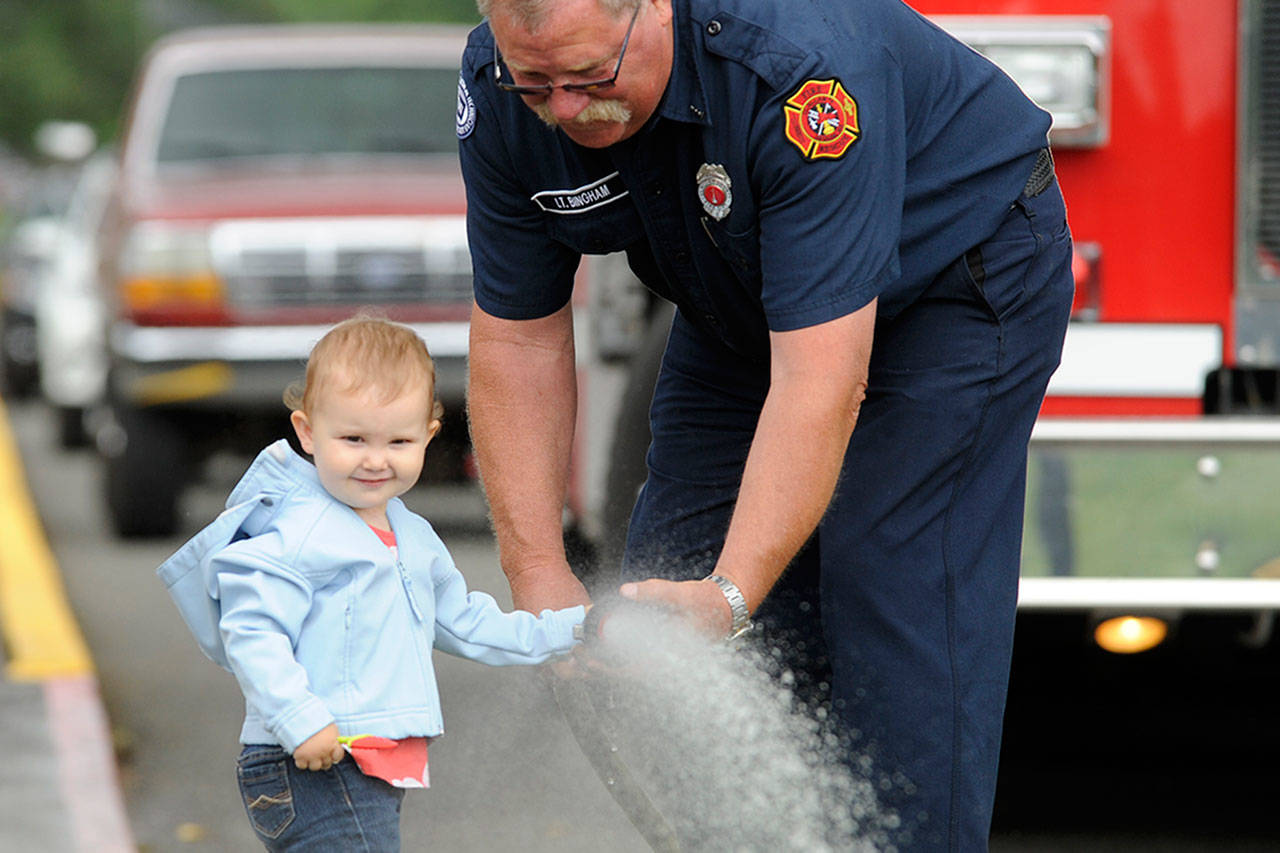 Lt. Lawrence Bingham with Clallam County Fire District 3 helps 19-month-old Lilly Allen shoot a firehose on July 11 after Firefighter Storytime through the Sequim Library. Sequim Gazette photo by Matthew Nash