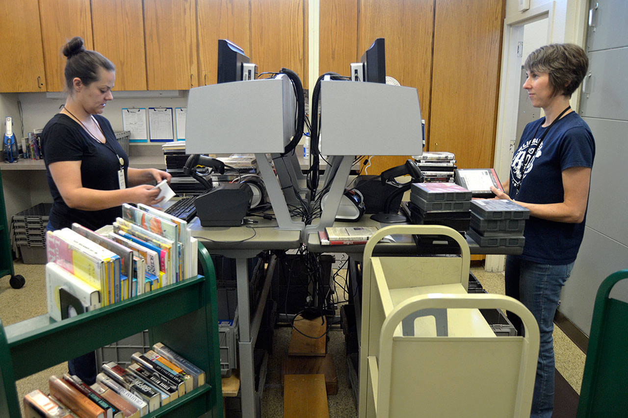 Annie Brooker, left, and Jessica Raivo, customer service specialists at the Sequim Library, check in books and movies recently returned or transferred to the branch. Effective Sept. 1, library staff stop late fines and fees for patrons to promote accessibility. Brooker said people shouldn’t be ashamed because staff often have late fees or fines because they see all the materials coming in and something new always catches their interest. Sequim Gazette photo by Matthew Nash