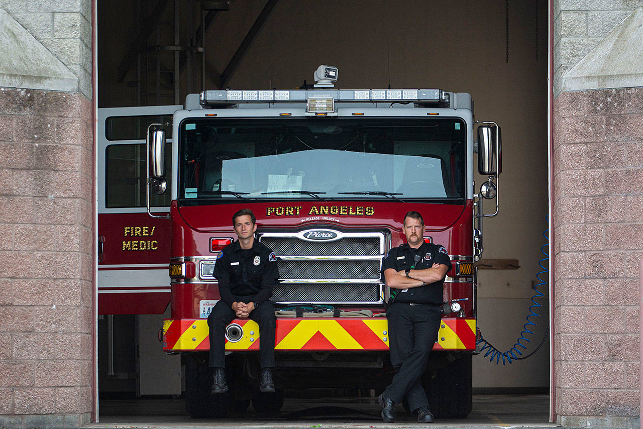 Port Angeles firefighter/paramedics Tyler Jacobson and Mark Karjalainen sit as American Legion Riders and bagpiper Rick McKenzie arrive to the Port Angeles Fire Department on the 18th anniversary of the 9/11 terrorist attacks Wednesday. (Jesse Major/Peninsula Daily News)