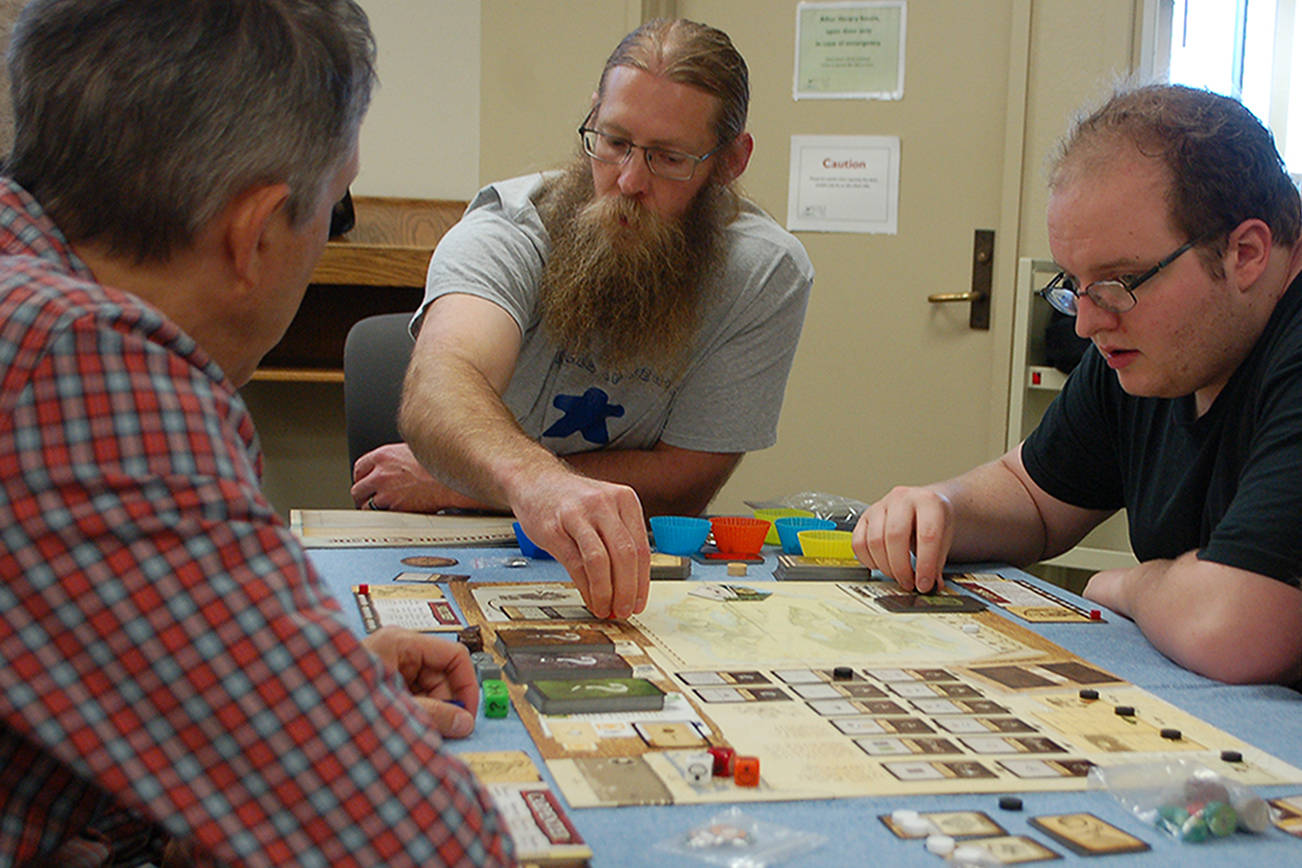 Travis Britten, second from left, demonstrates how to play the board game “Robinson Crusoe” to several Meeples of Sequim regulars who hadn’t yet played it. Britten says that he regularly brings new games to teach as that kind of experience is a big part of gaming for him. Sequim Gazette photo by Conor Dowley