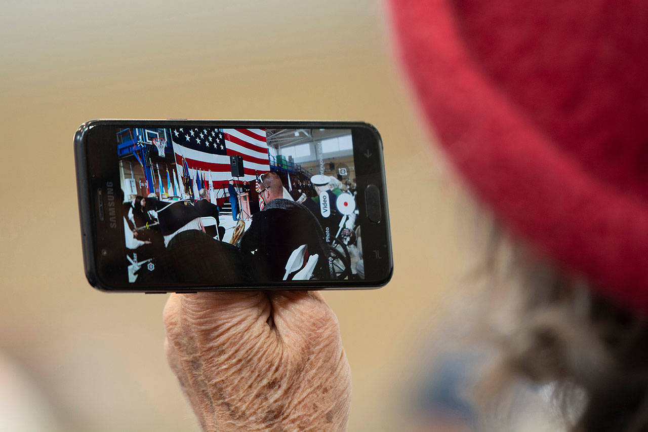 A woman records video of Members of the Mount Olympus Detachment of the Marine Corps League perform a three-volley rifle salute at the Veterans Day ceremony at U.S. Coast Guard Air Station/Sector Field Office Port Angeles on Monday. (Jesse Major/Peninsula Daily News)
