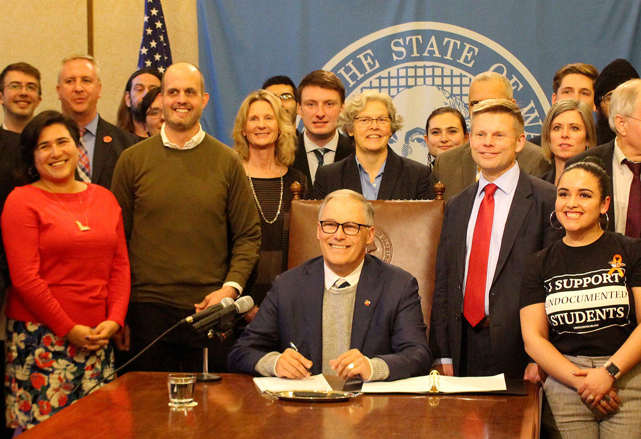 Gov. Jay Inslee, seated, signs the first bill of the 2020 legislative session into law. On the right stands the bill’s primary sponsor, Sen. Jamie Pedersen, D-Seattle, who is wearing a red tie. Photo by Cameron Sheppard/WNPA News Service
