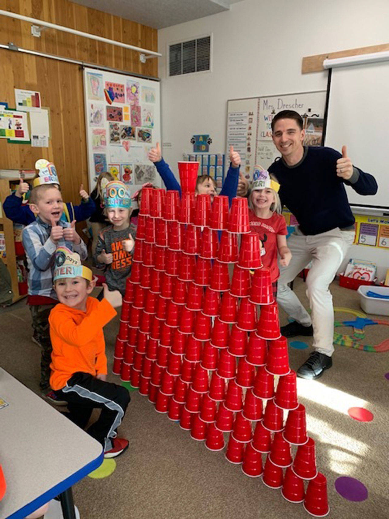 Greywolf kindergarten students Carter Gillaspy, A.J. Lawson, Mason Endicott, Lucas Windrich, and Nevaeh McNeill — pictured here with teacher Sean O’Mera — celebrate the 100th day of school by stacking 100 cups. Photo by Carla Drescher