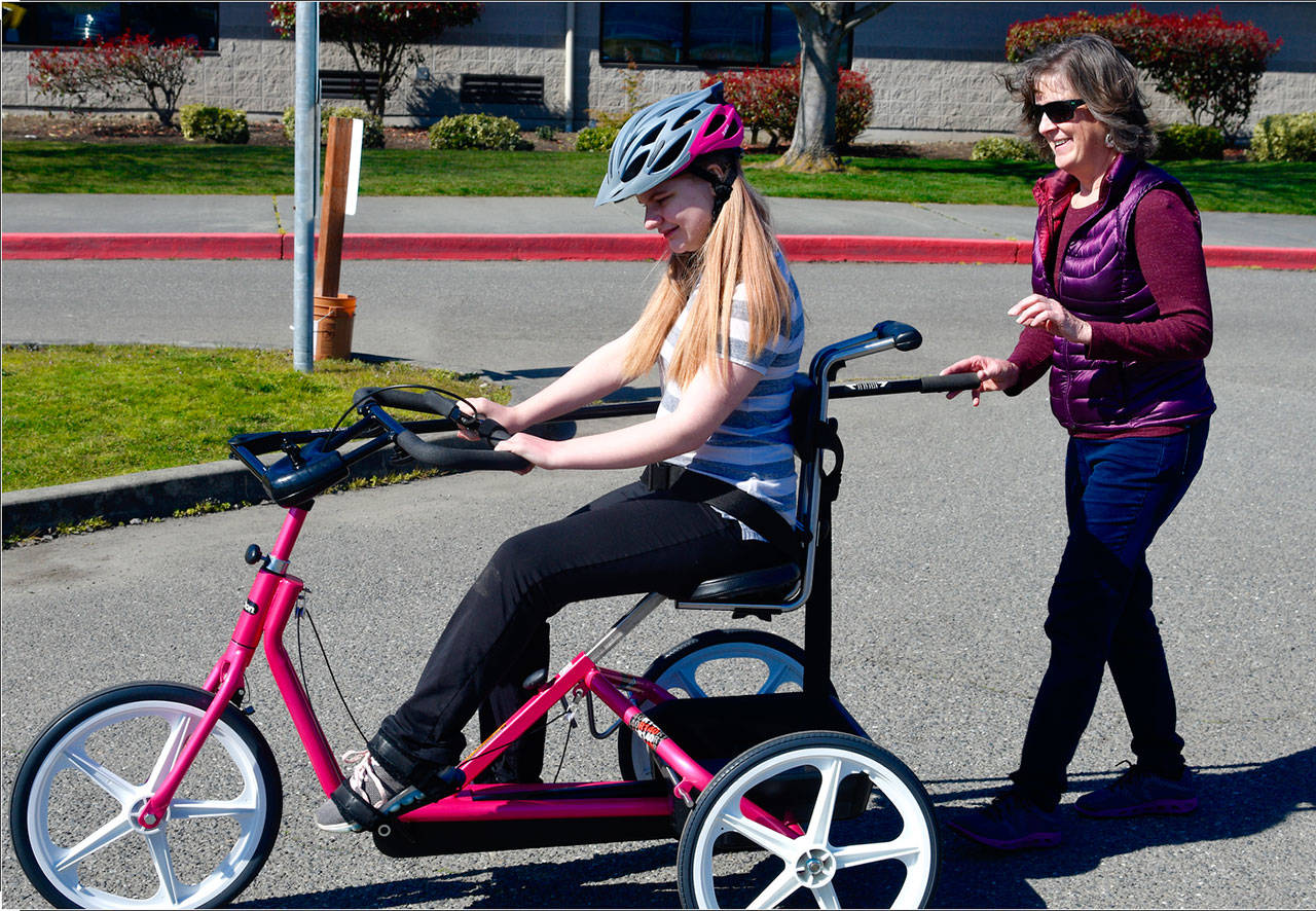Alina Grieb, enjoys a ride on her new bike as physical therapist Cheri Bibler assists. Photo by Doug Schwartz