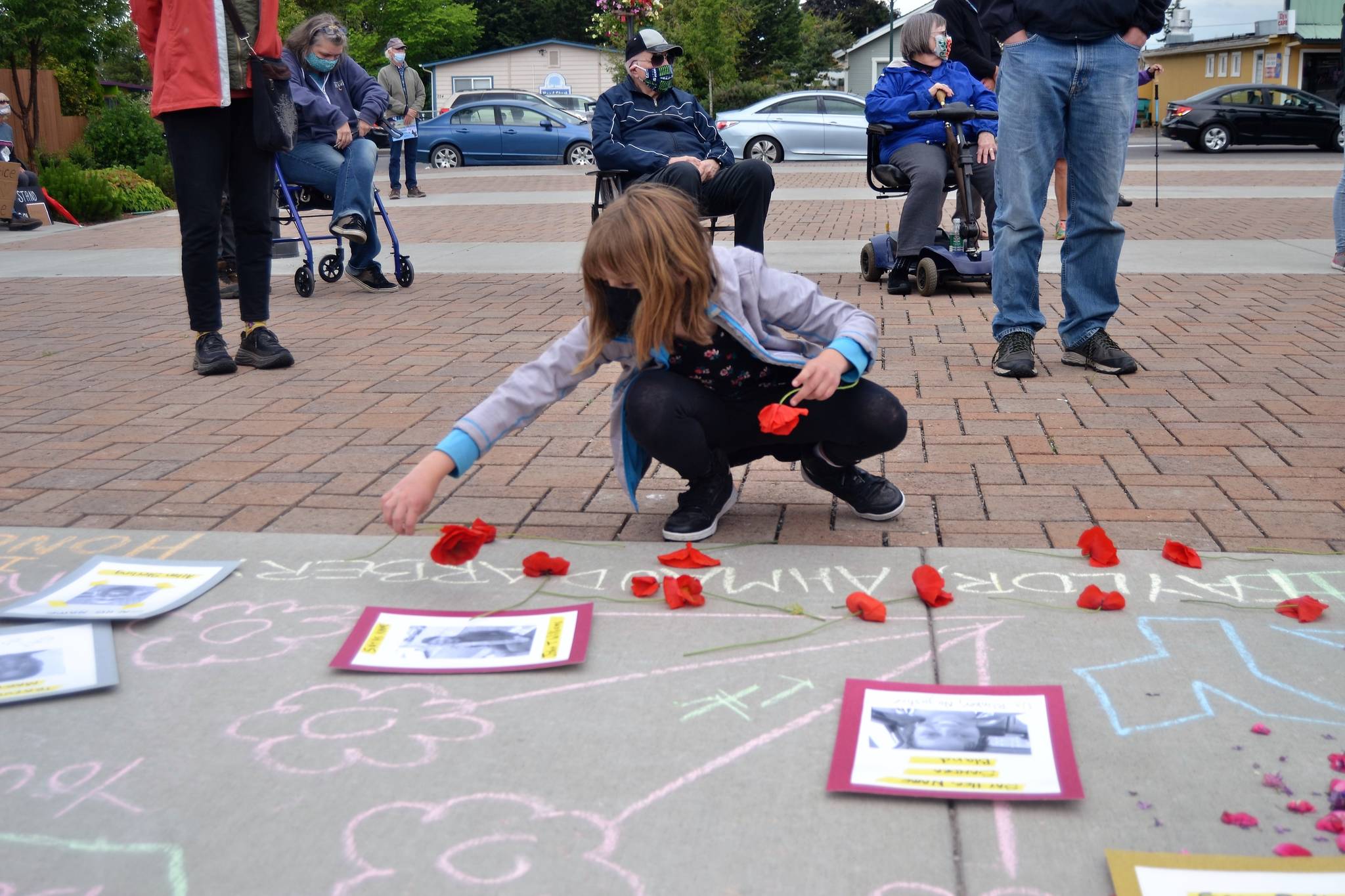 Eleven-year-old Maisy French of Sequim places flowers down by pictures of black people victimized by police brutality on June 5 at the Sequim Civic Center. She participated in the vigil with her parents and brother with her mom Tammy saying they participated because they wanted to make sure something is done about the violence occurring in the nation.
