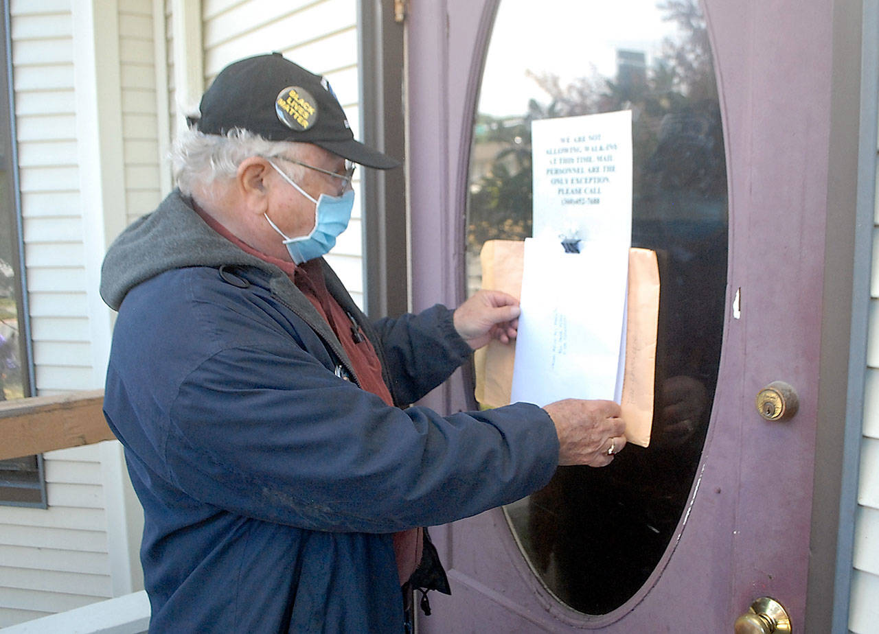 Tim Wheeler of Sequim, acting chairman of the non-partisan Voices for Health and Healing, attaches an envelope containing a letter on the front door of the building housing the Port Angeles office of U.S. Rep. Derek Kilmer on Thursday, July 23. The letter, signed by reportedly some 120 people, expressed disappointment in Kilmer’s progress in promoting universal health care, protection of Social Security and efforts to contain military spending, in particular the expansion of the U.S. Navy’s Growler aircraft training program at Naval Air Station Whidbey Island. Photo by Keith Thorpe/Olympic Peninsula News Group