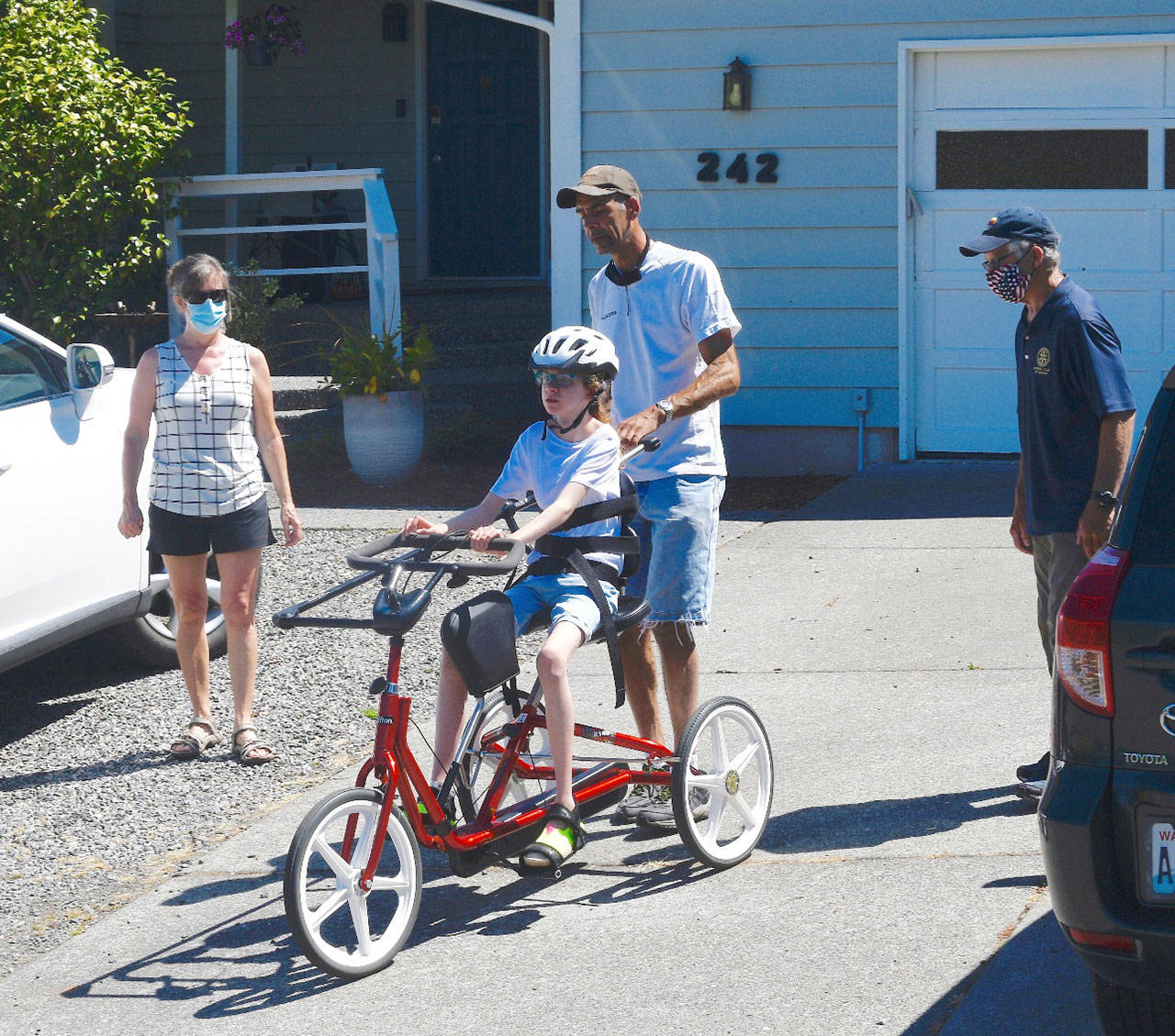 With Cherry Bibler, Sequim School District physical therapist (left) and Sequim Noon Rotary member Bob Macaulay (right) looking on, 11-year-old Abby Johnson takes a rides on her adaptive bike — with new steering bar — with help from her father, Alvin Pitts. Photo by Doug Schwarz
