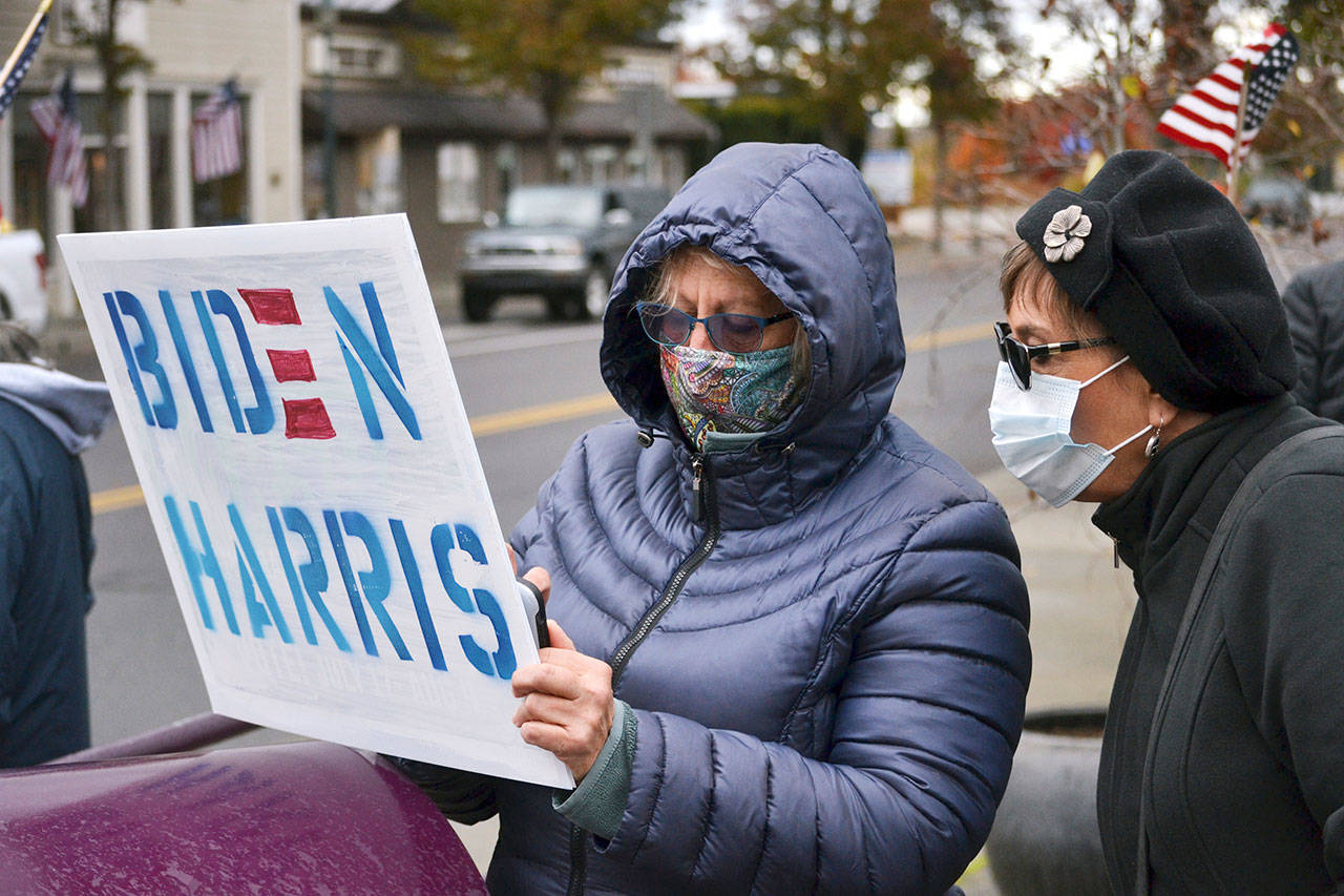 Kathy McGee and Chris Walker, both of Sequim, look at updated news on the presidential election on Nov. 7 as they rally with other community members to show their support for the election of Joe Biden and Kamala Harris. Sequim Gazette photo by Matthew Nash