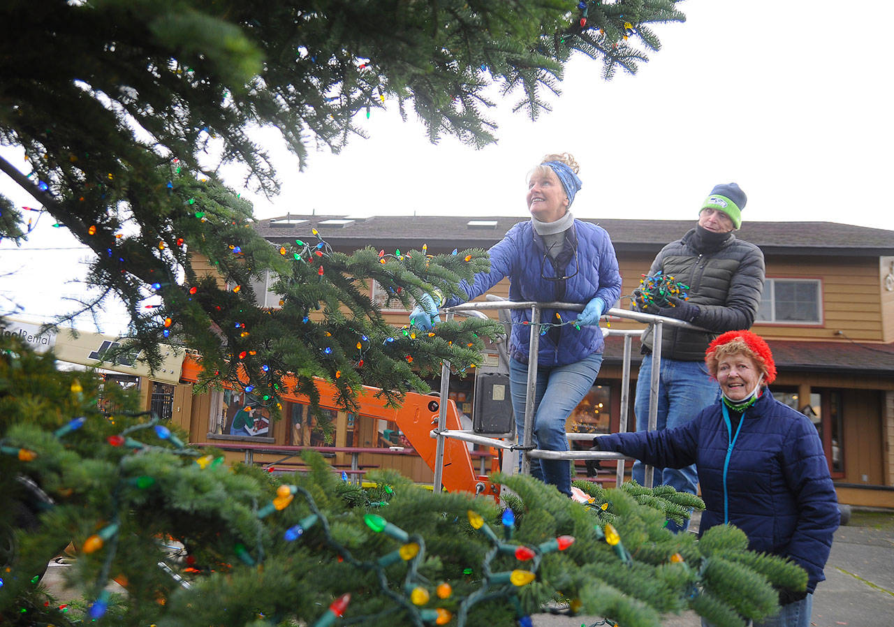 Captain-Crystal Stout, Emily Westcott and Terry Marsh add some seasonal flair to the Christmas/holiday tree at Centennial Place in downtown Sequim last week. Sequim Gazette photo by Michael Dashiell