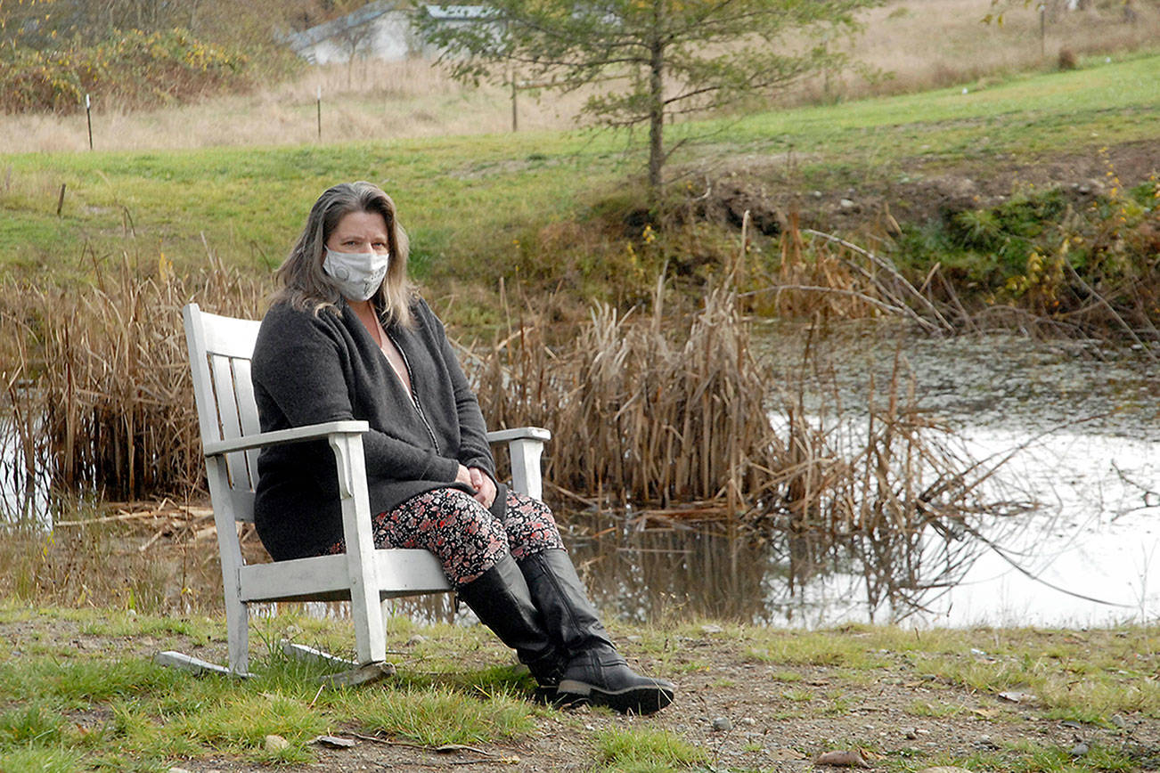 Keith Thorpe/Peninsula Daily News
Nurse and COVID-19 survivor Laura Dotlich sits next to a small pond at her home in rural Port Angeles on Thursday.