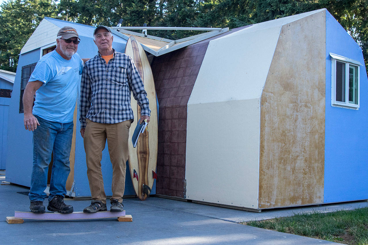 Brad Griffith and Gary Young demonstrate the strength of their modular shelter panels outside the demo version in Sequim. Behind Young is one of his fiberglass-free surfboards. Sequim Gazette photo by Emily Matthiessen