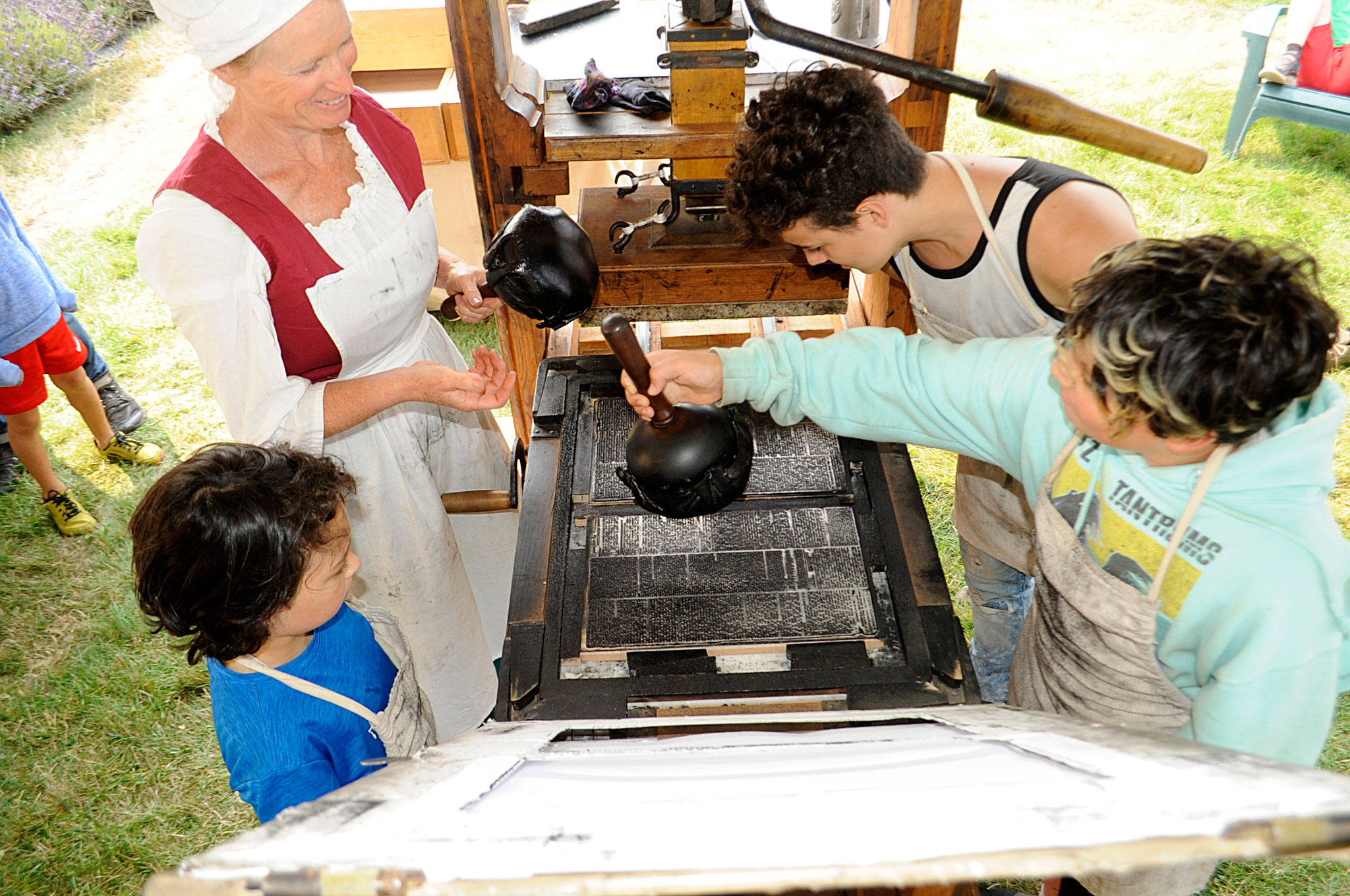 Nickie Allen of Utah shows brothers Rizzolo, 9, Canaan, 12, and Broden Texeira, 17 of Bremerton how her husband Gove’s replica of Isaiah Thomas’ printing press works. The Allens returned to the Northwest Colonial Festival for the first time since 2017 to share hands-on learning.