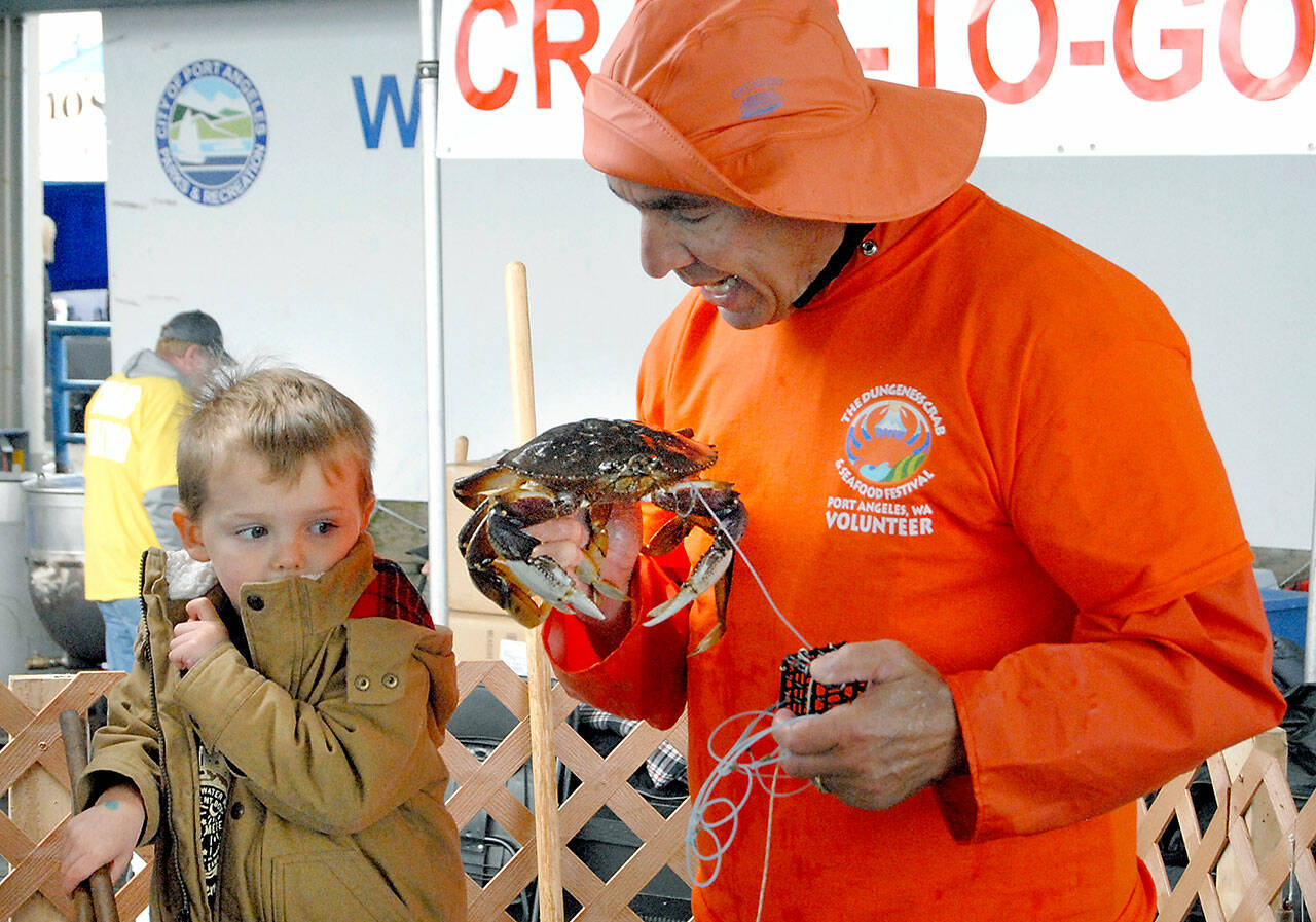 In 2019, Hayden Fuller of Seabeck gives a wary look as Robert Rohner of Sequim, a member of the North Olympic Peninsula Chapter of Puget Sound Anglers, gives the youngster a close up view of the crab he just caught during Saturday’s crab derby at Port Angeles City Pier, a featured event of the Dungeness Crab and Seafood Festival. File photo by Keith Thorpe/Olympic Peninsula News Group