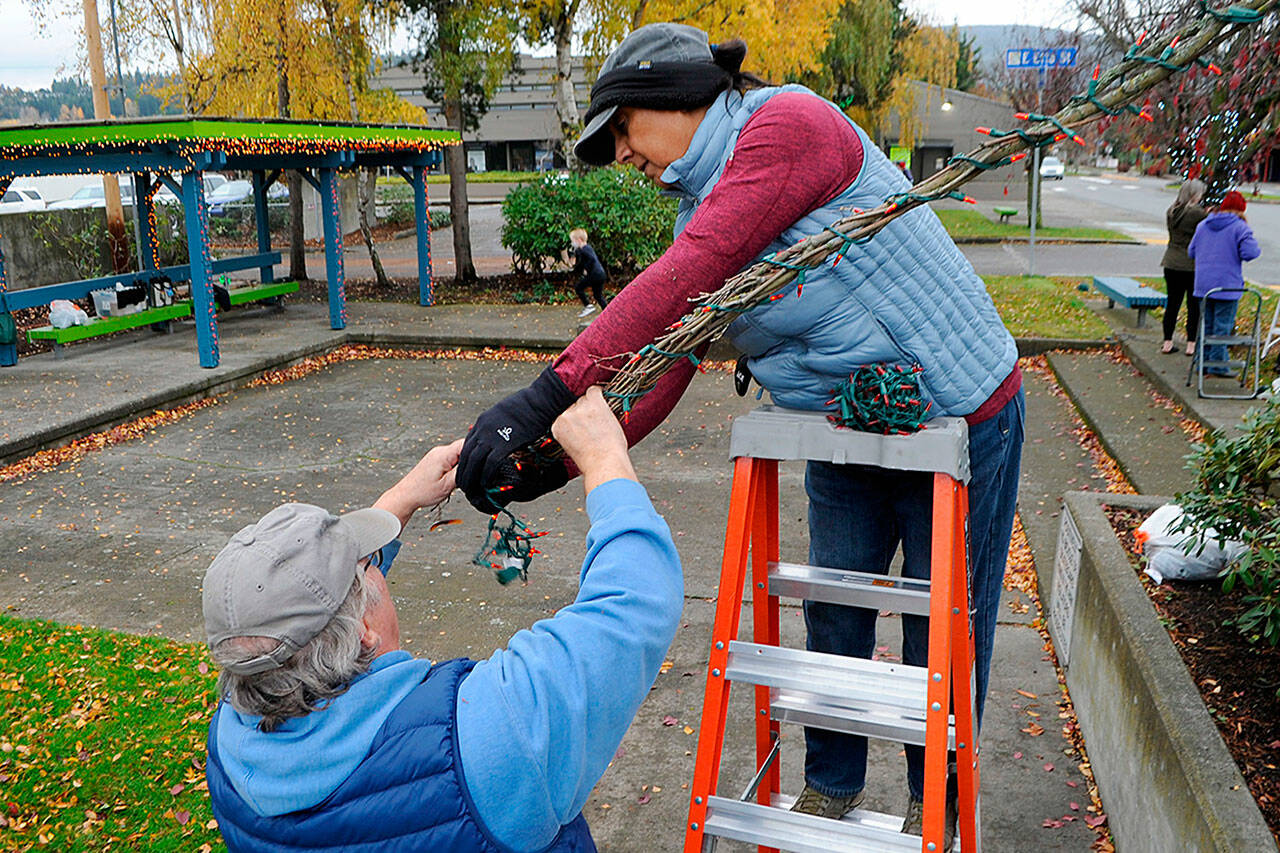 Mike and Ester De Weese of Sequim help each other wrap a tree branch in Christmas lights on Nov. 13 by 1st Security Bank. They typically help fellow volunteer Captain-Crystal Stout and the Dreamcatcher Balloon program, and wanted to help her decorate downtown, too. Sequim Gazette photos by Matthew Nash