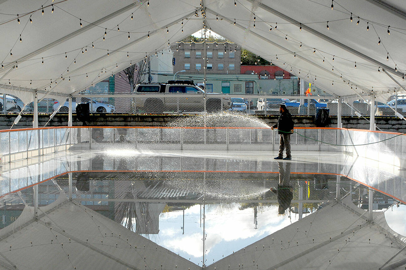 Shawn Kidwell, an employee of Ice-America, a California-based company that rents portable ice rinks, applies water on Tuesday to the refrigerated surface of a temporary rink that will be the highlight of the Port Angeles Winter Ice Village. (Keith Thorpe/Peninsula Daily News)