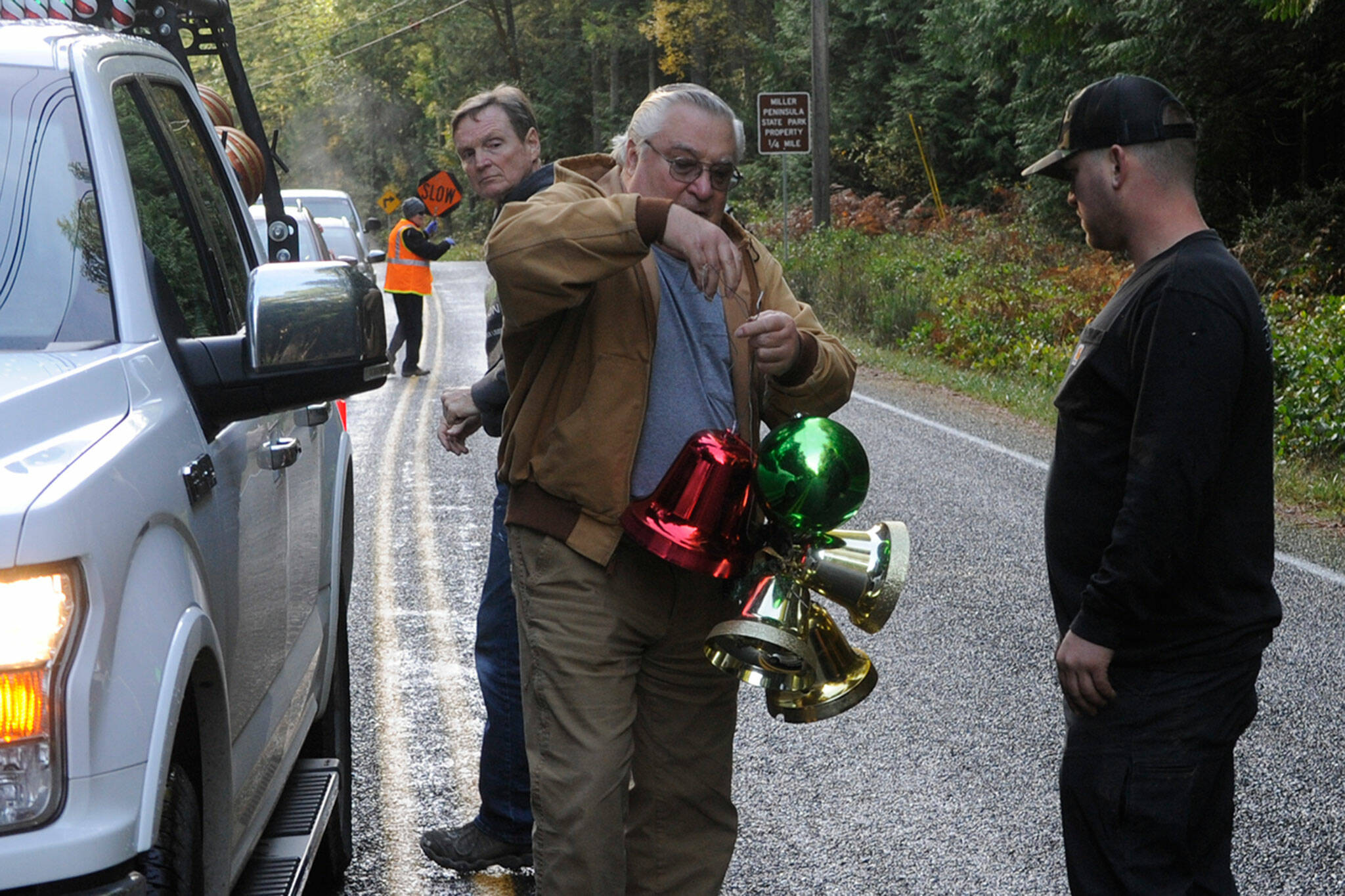 Kent Bohac hands decorative bells to Will Sullivan to place in trees along Diamond Point Road on Nov. 20 as Craig Tenhoff looks on. Sequim Gazette photo by Matthew Nash