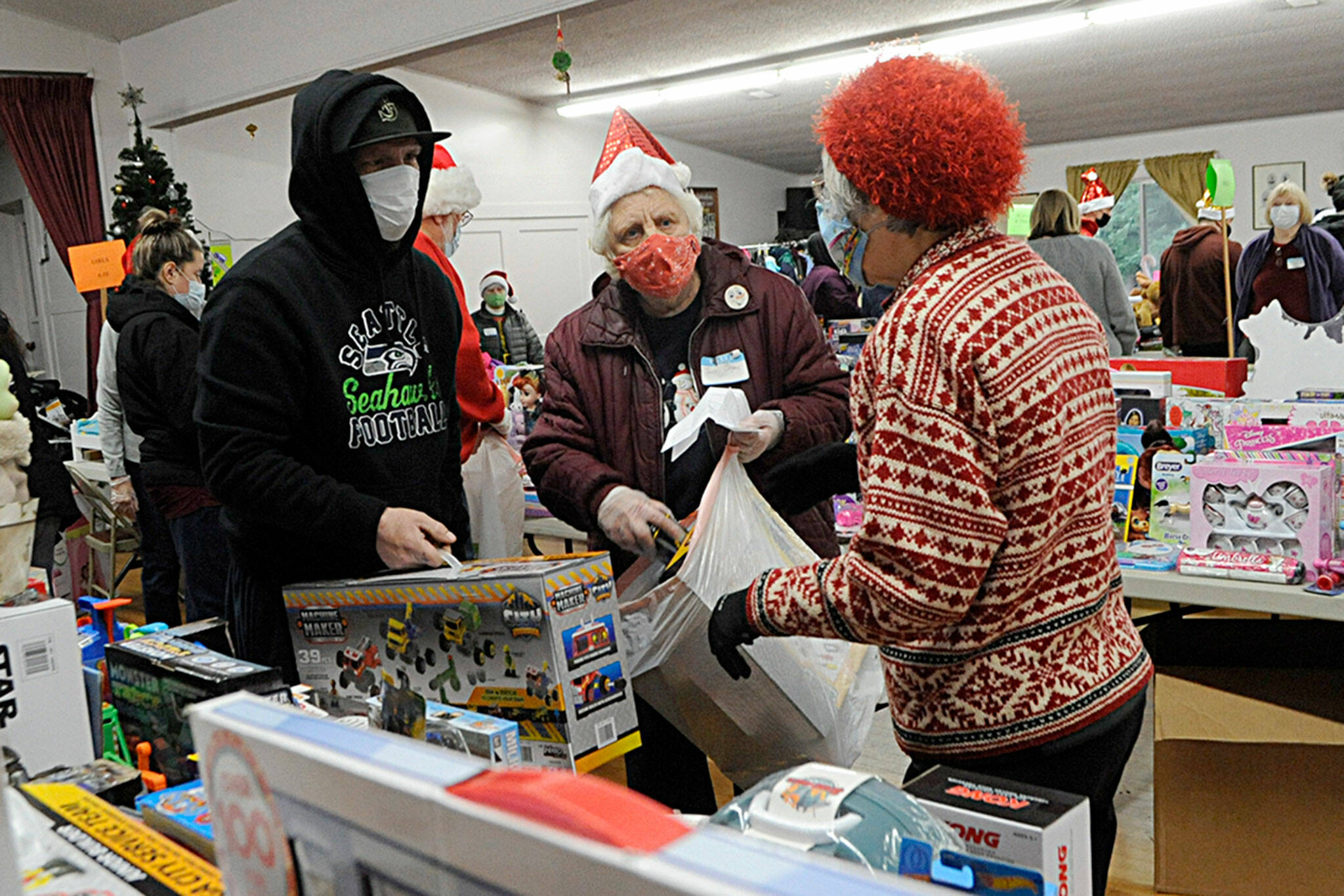 Sequim Community Aid volunteers Jean deJong and Pat Gritman help Ken Glen find the right toys for his four children at Toys for Sequim Kids on Dec. 15. Sequim Gazette photo by Matthew Nash