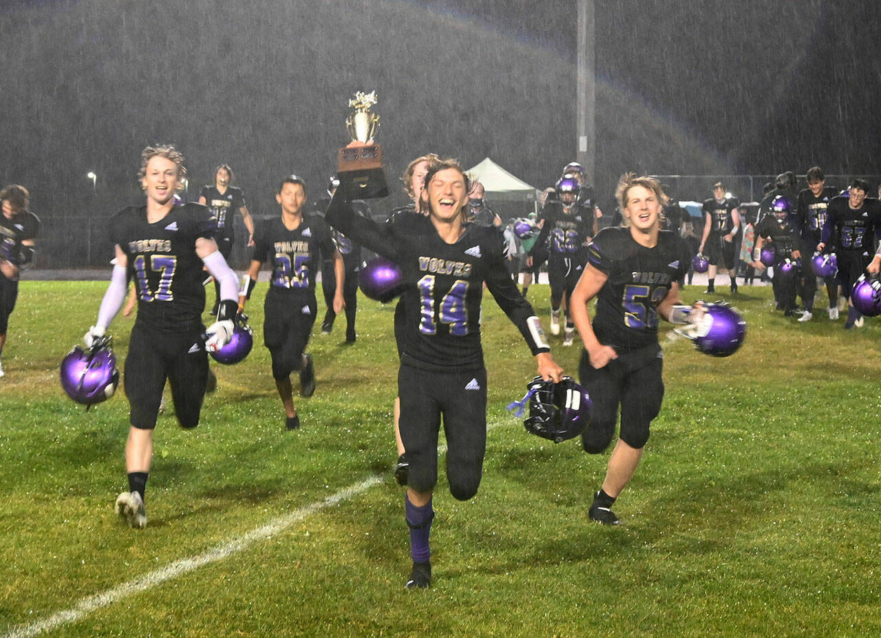 Sequim Gazette photos by Michael Dashiell
Above: Sequim’s Kobe Applegate holds the Rainshadow Rumble rivalry trophy as the team heads toward the student section to sing the school fight song after a 17-12 win over Port Angeles on Sept. 17. Below: Sequim’s Kendall Hastings, center, looks to hit past the block of Lillian Halberg, left, and Karma Williams in the Wolves’3-1 win over their rivals on Sept. 9.