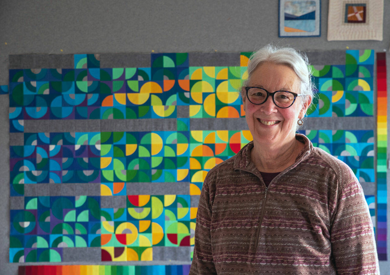 Fiber Artist Marla Varner stands in front of her temperature quilt. Each square is color coded to the high and low temperatures of each day of 2021 in her neighborhood in Sequim, with the smallest quarter circles signifying precipitation. Sequim Gazette photo by Emily Matthiessen